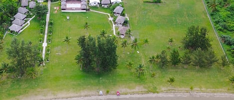 Vista aérea de un resort con varias construcciones, un extenso césped con palmeras y una playa.