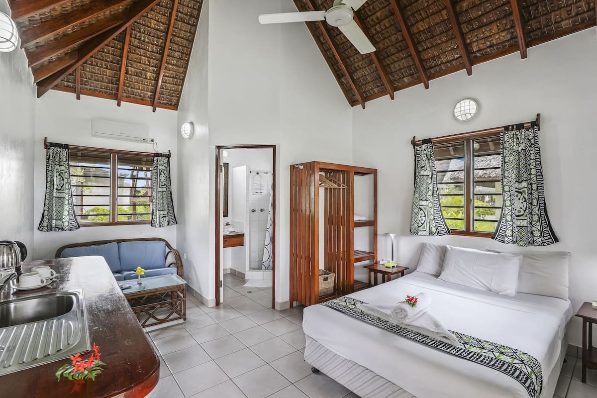 A hotel room with a bed, a sofa, a dining table, a shower, and a window with patterned curtains.