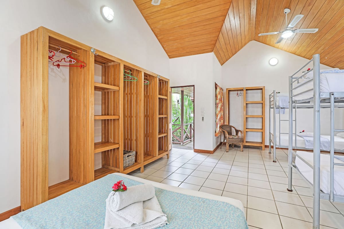 A room with a bed, wooden wardrobe, bunk beds, and a ceiling fan.
