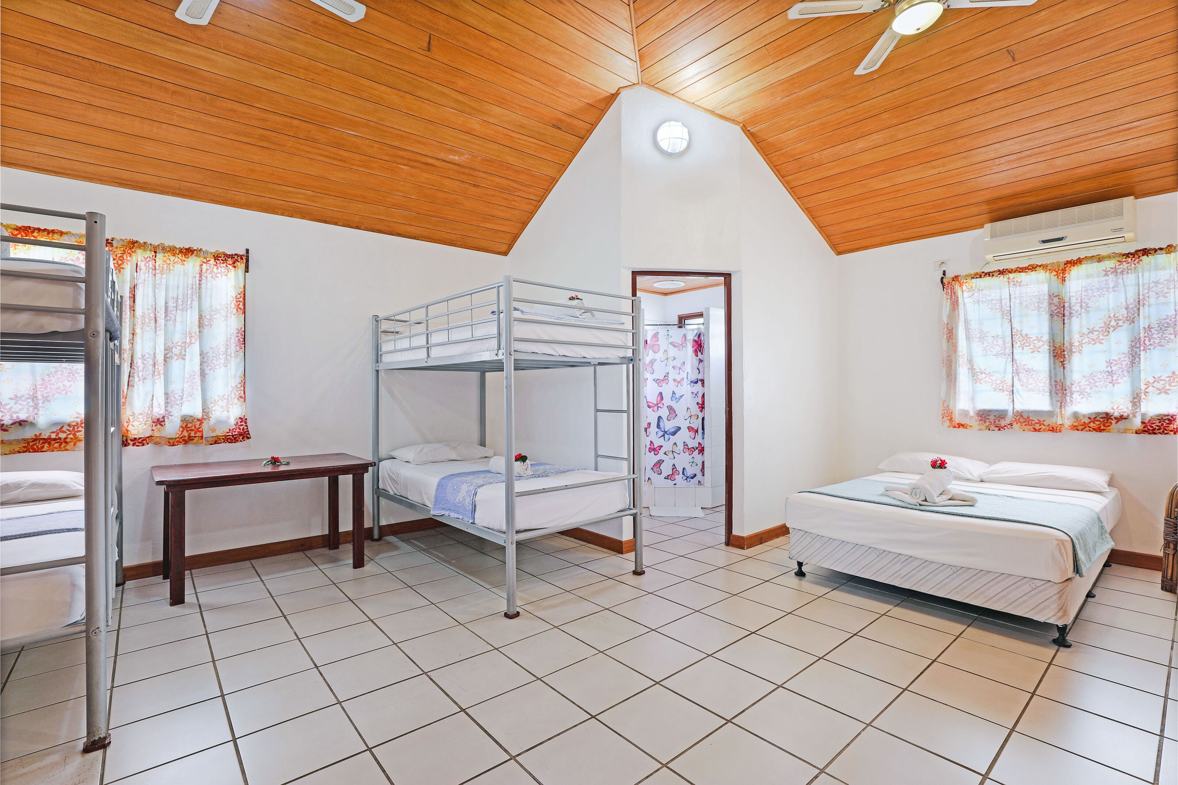 A dormitory room with bunk beds, a desk, and a window with curtains.