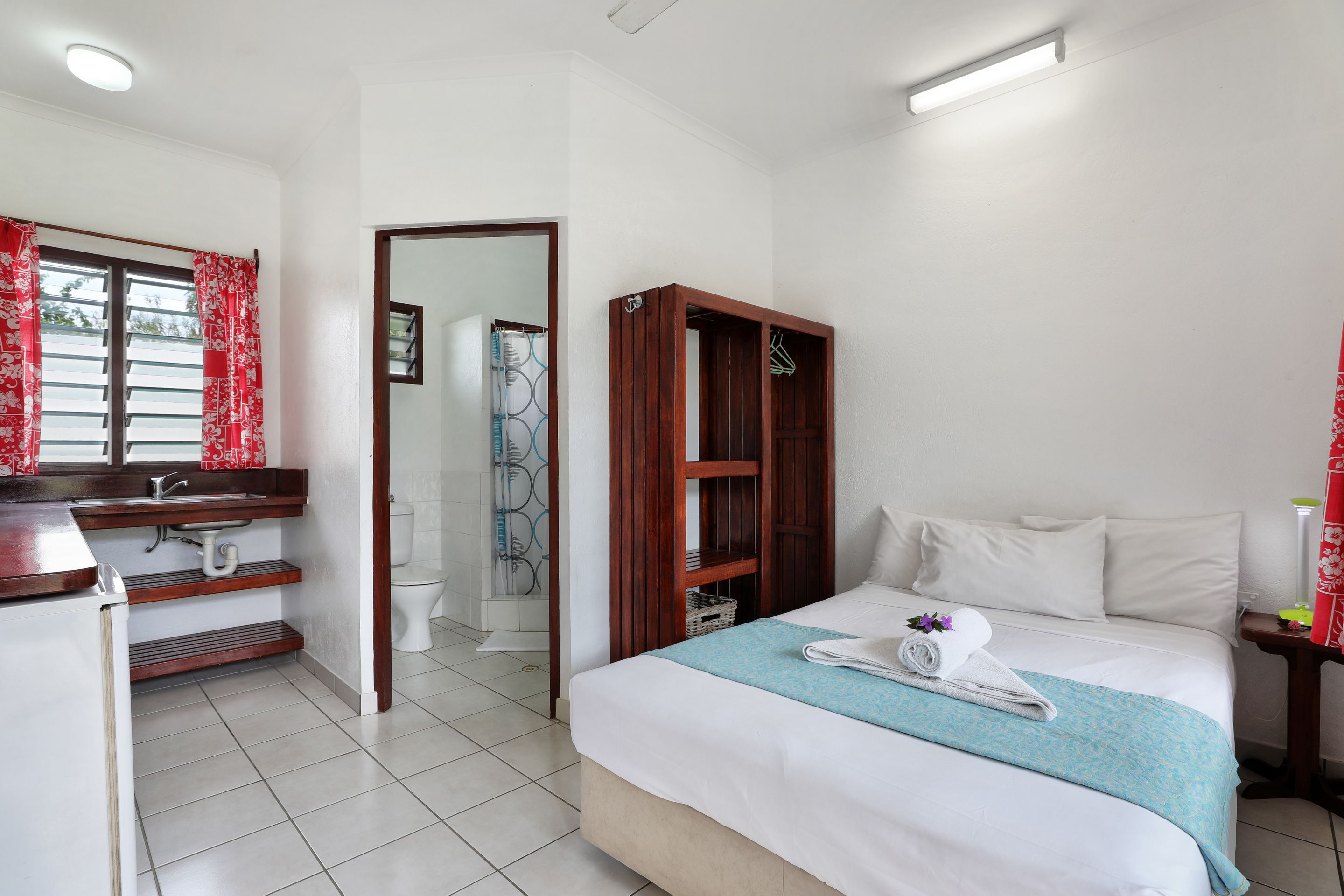 Une chambre d’hôtel comprenant un lit, une armoire en bois, une salle de bain avec douche et un lavabo.