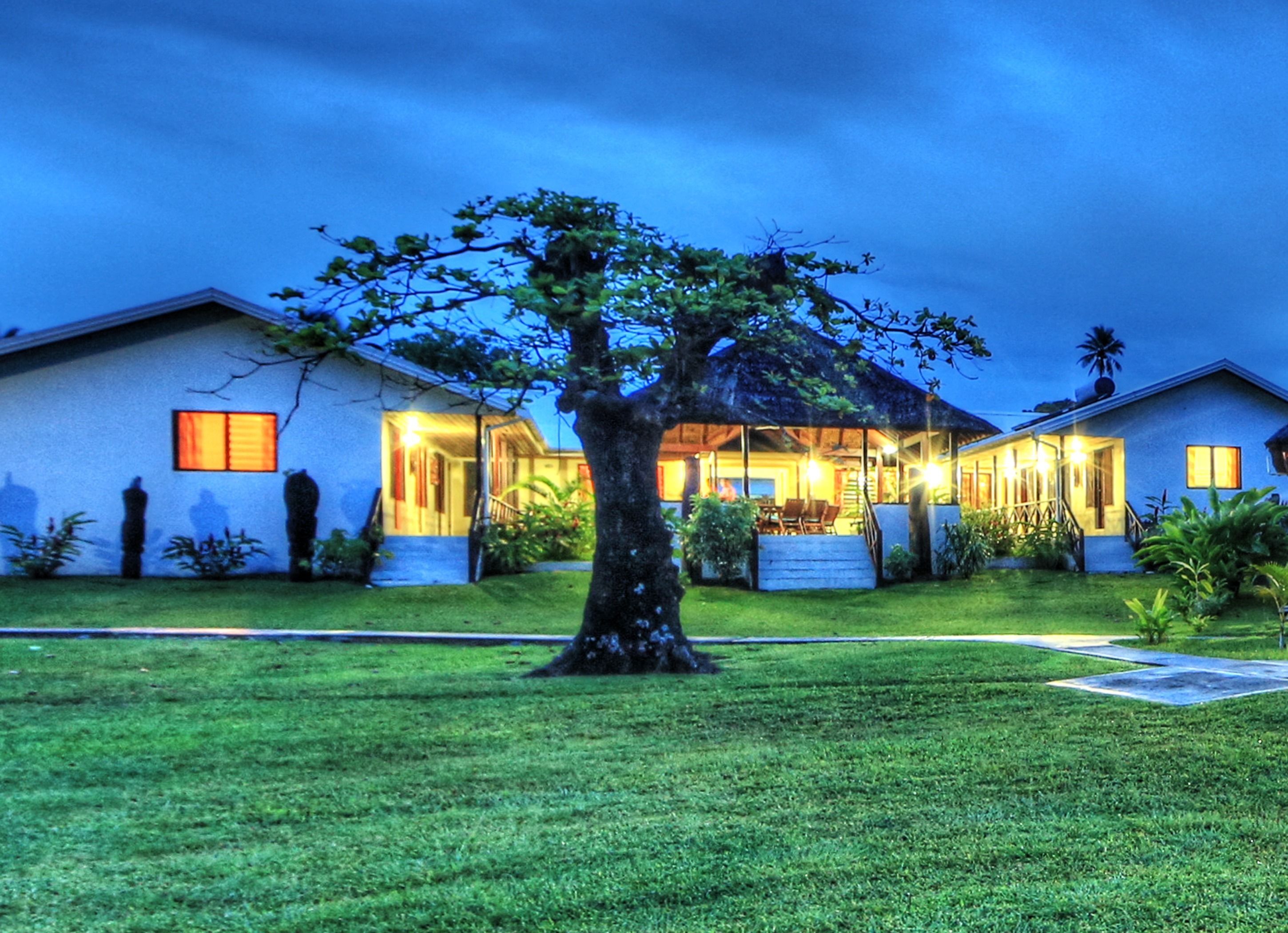 A two-story house with a covered outdoor area, a lawn, and a tree in the foreground.