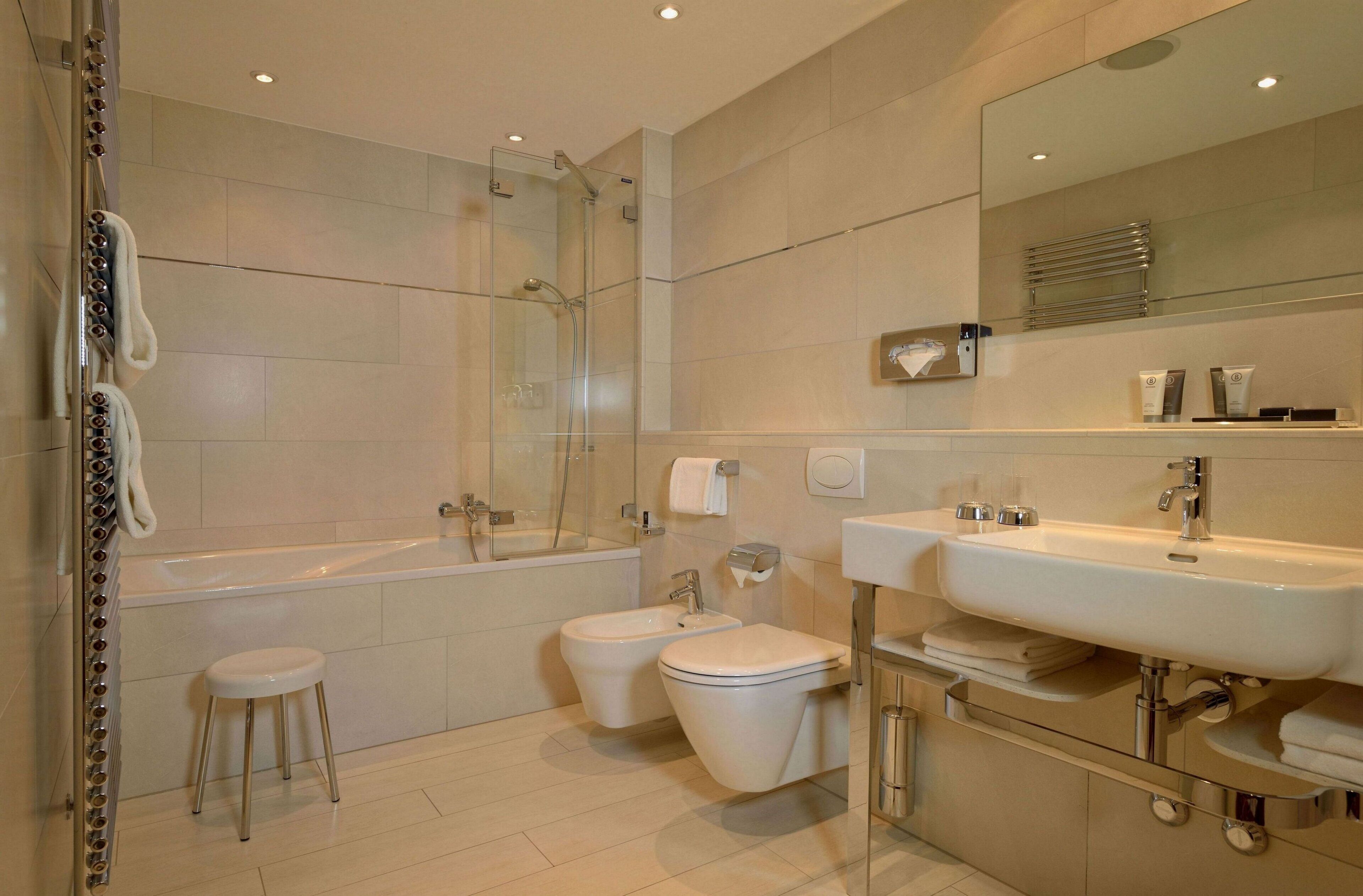 A modern bathroom with a bathtub, two toilets, a bidet, a sink, and a glass shower enclosure.