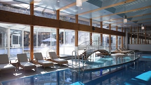 A modern indoor swimming pool with glass walls, lounge chairs, and a staircase leading to upper levels. - Hotel Monte Rosa (Zermatt)