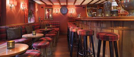 A bar area with red plaid seating, a wooden bar counter, and a clock on the wall.