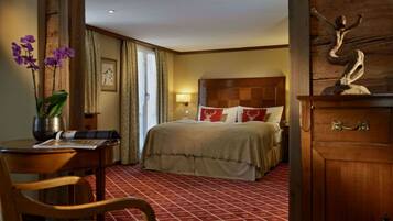 Une chambre d’hôtel avec un lit, une armoire en bois, un bureau avec une chaise et un vase rempli de fleurs.