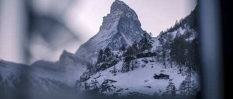 A mountain with a prominent peak, surrounded by snow-covered trees and a small building at its base.
