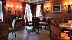 A cozy room with wooden ceiling beams, a fireplace, a dining table with chairs, and a sofa. - Hotel Monte Rosa (Zermatt)