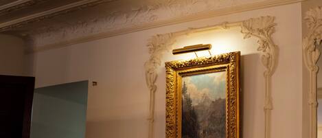 A framed painting with a gold frame, mounted on a wall with ornate molding.