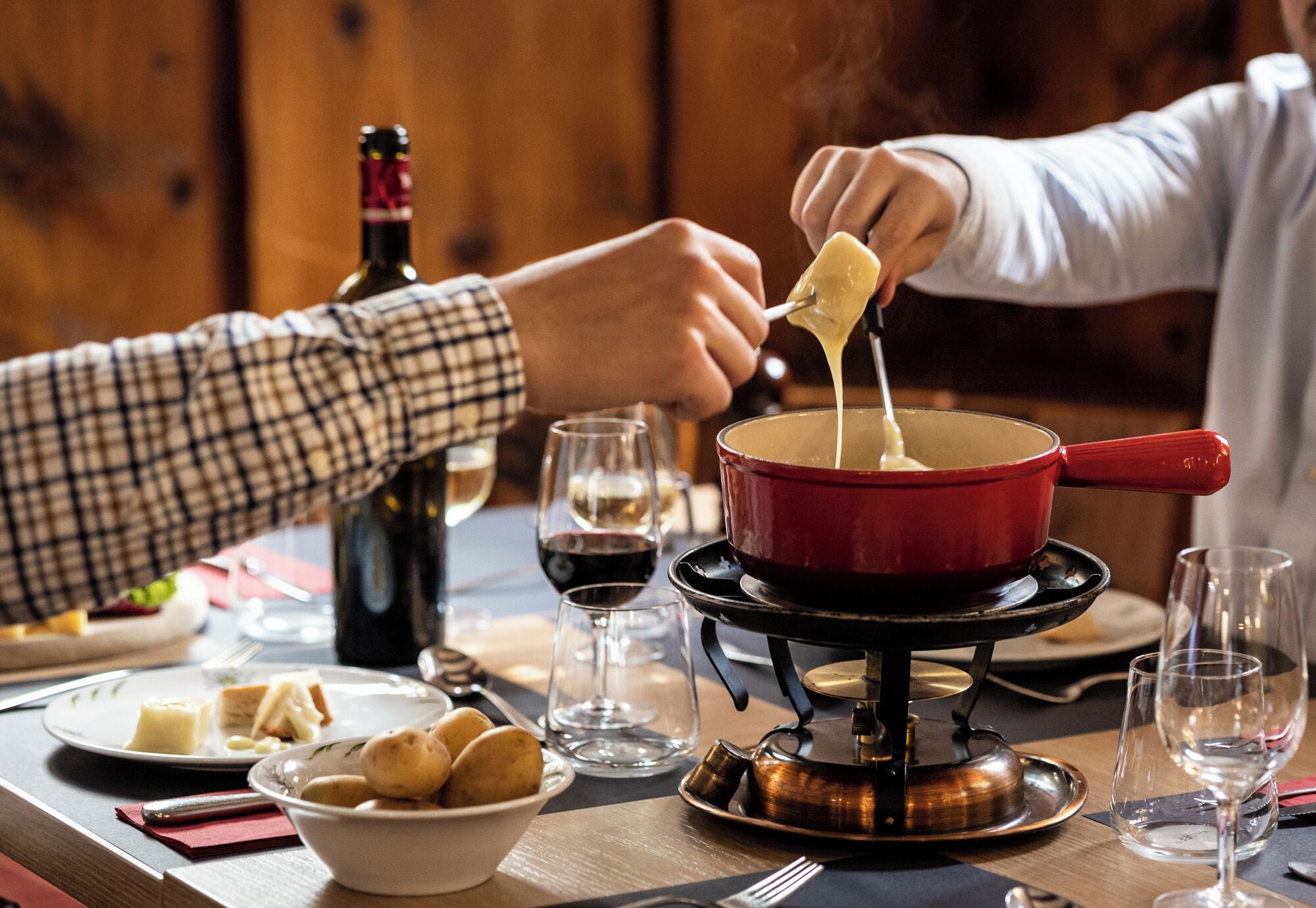 A dining table with a fondue pot, wine glasses, and plates of food.