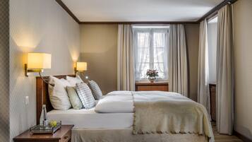 Une chambre d’hôtel avec un lit bien fait, deux lampes de chevet, une table de chevet avec une lampe et une fenêtre avec des rideaux.