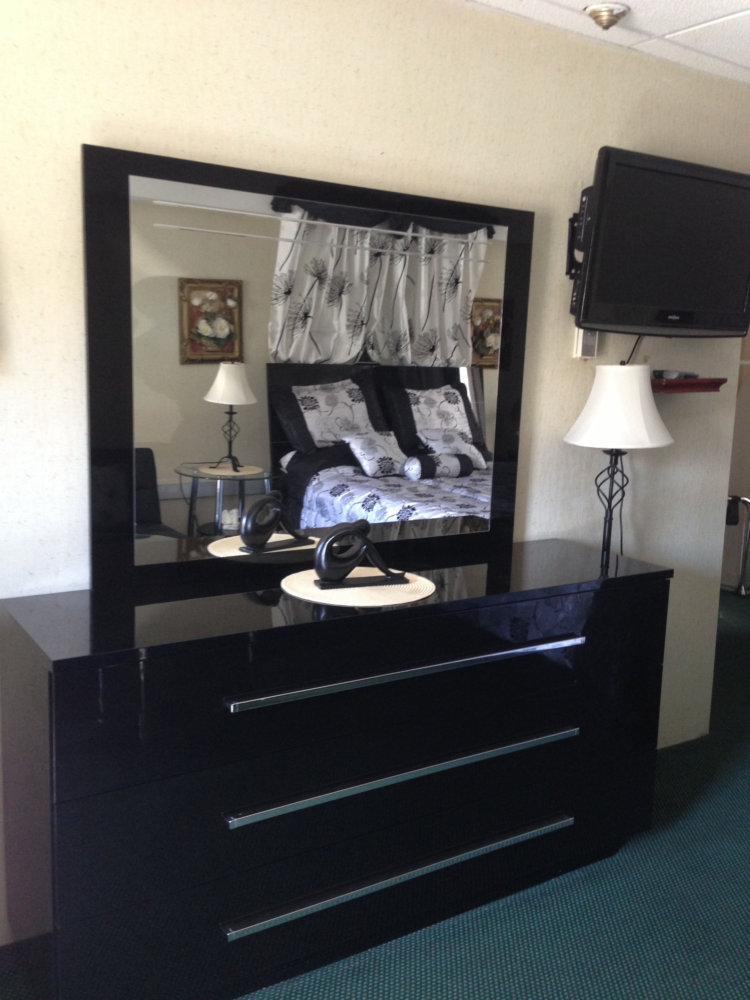 A hotel room with a large bed, a mirror, a TV, a desk, and a lamp.