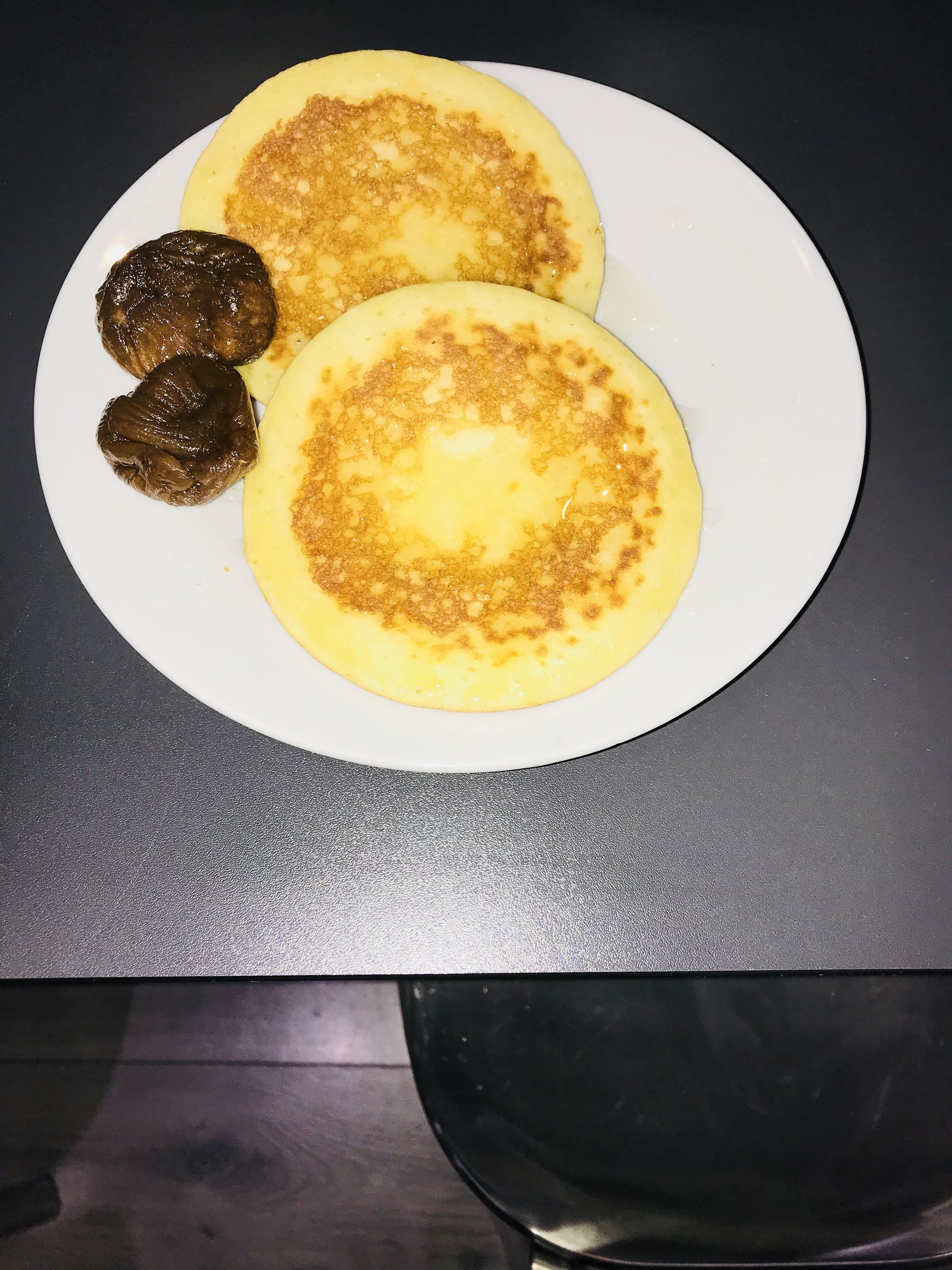 Un plato con dos tortitas y dos elementos marrón oscuro, posiblemente albóndigas, sobre una superficie oscura.