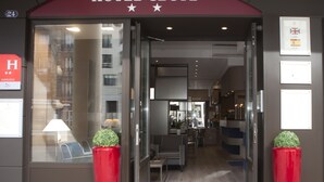 The entrance to Hotel Cecyl with a modern design, featuring a glass door, red planters, and a visible interior with seating and a counter. - Hotel Cecyl Reims Centre (Reims)
