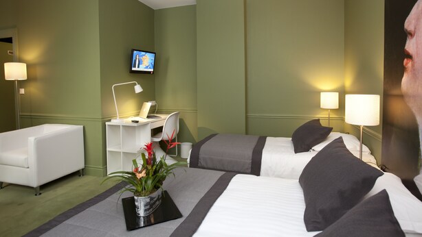 A hotel room with two beds, a desk, a chair, a TV, and a potted plant. - Hotel Cecyl Reims Centre (Reims)