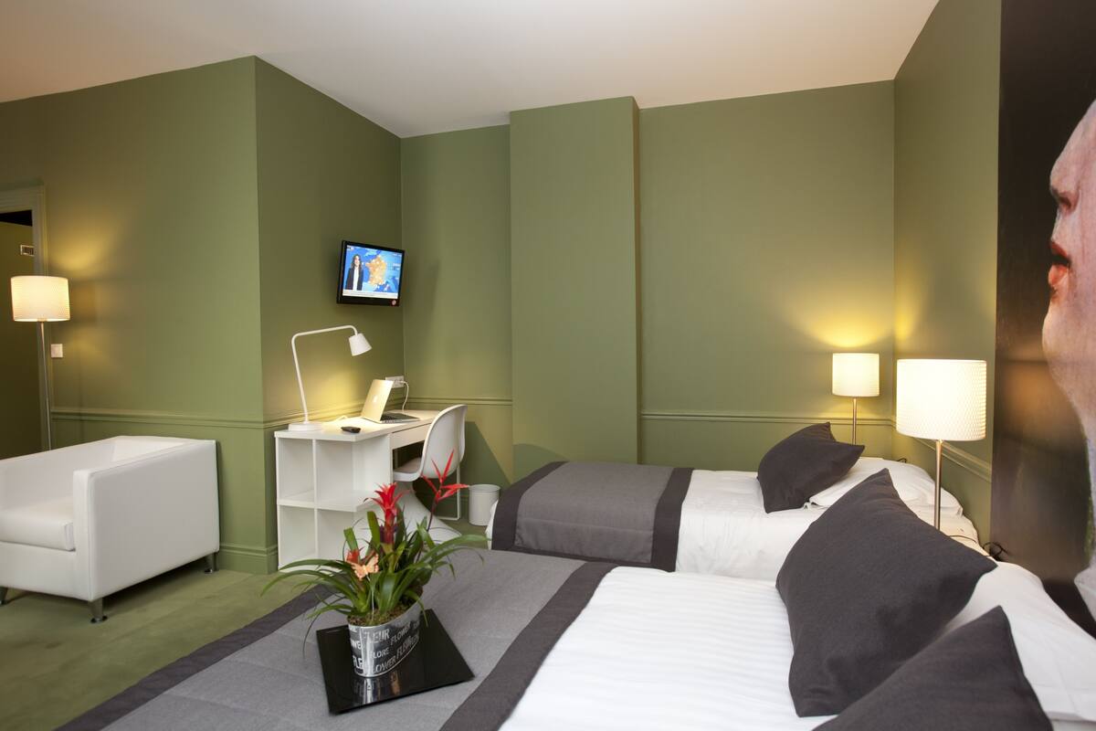 Habitación de hotel con dos camas, un escritorio, una silla, un televisor y una planta en maceta.