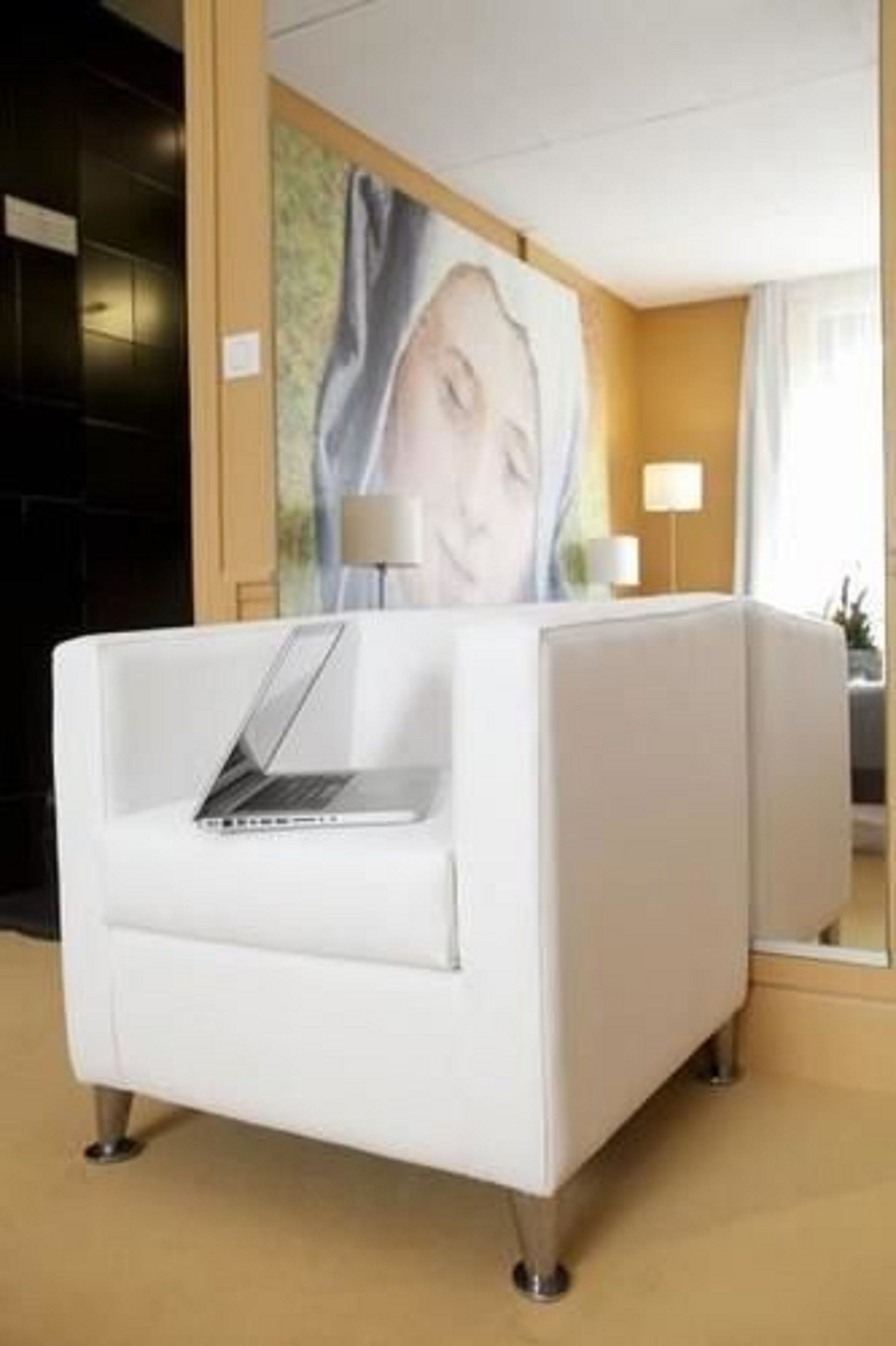 A white sofa with a laptop, a painting on the wall, and a lamp.