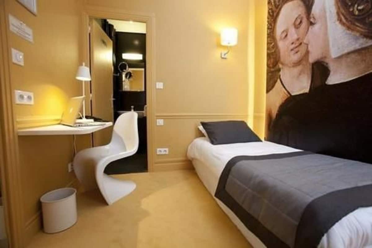 Una habitación de hotel con cama, escritorio, silla y lámpara de pared.
