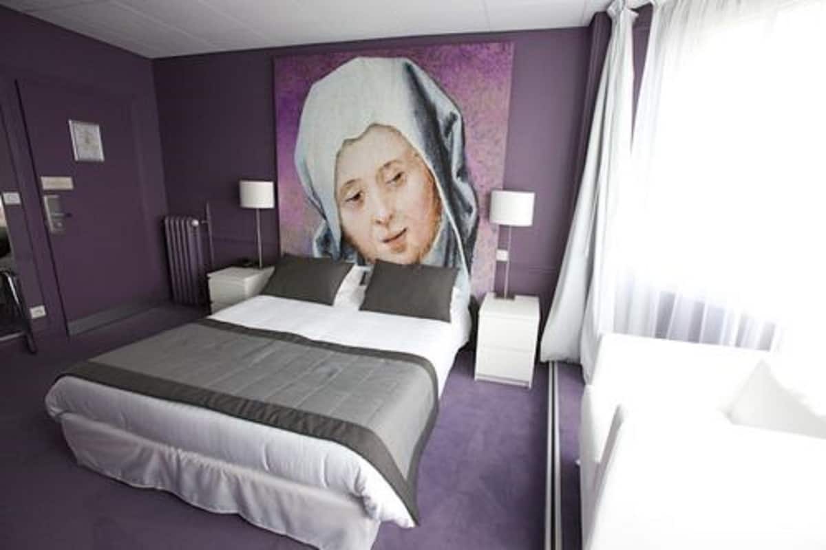 Habitación de hotel con una cama grande, dos mesitas de noche, una lámpara y un ventanal con cortinas.