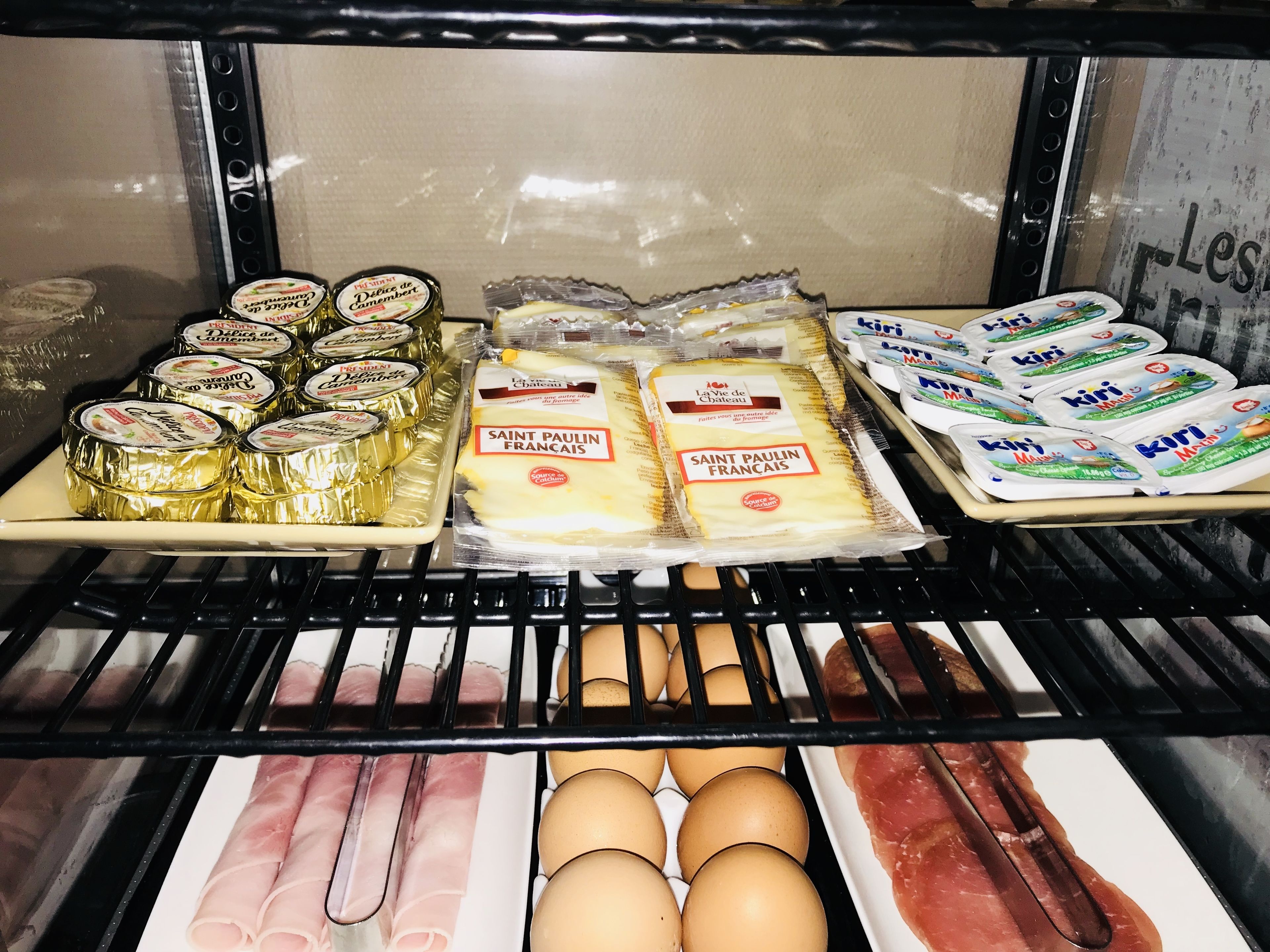 Mostrador refrigerado con varios alimentos, entre ellos queso, yogur y huevos.