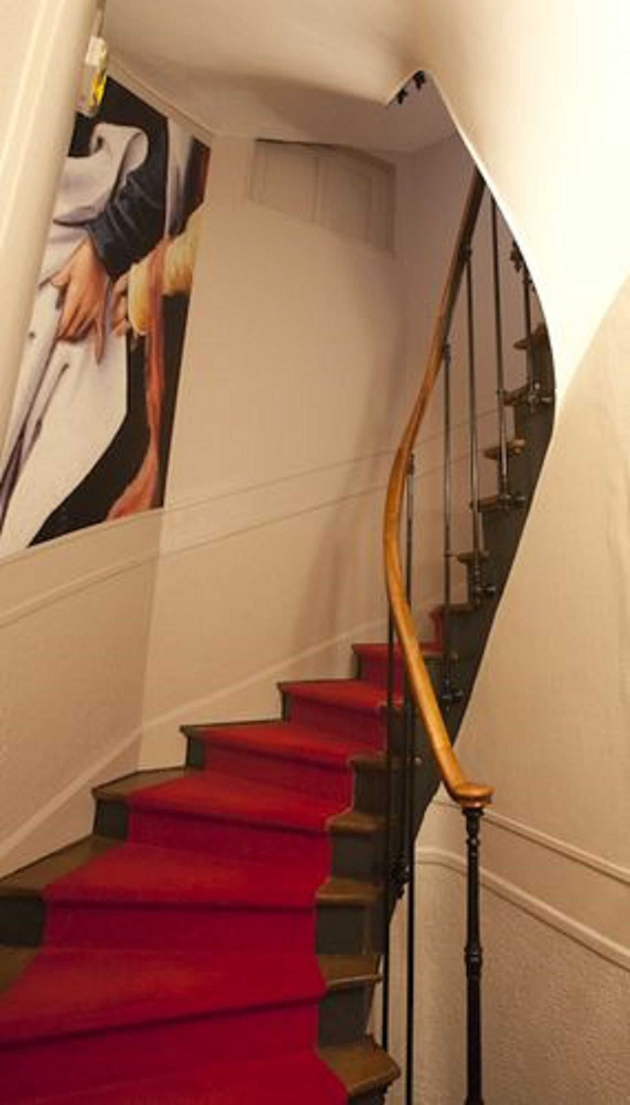 Un escalier dont les marches sont recouvertes d’une moquette rouge et qui possède une main courante en bois.