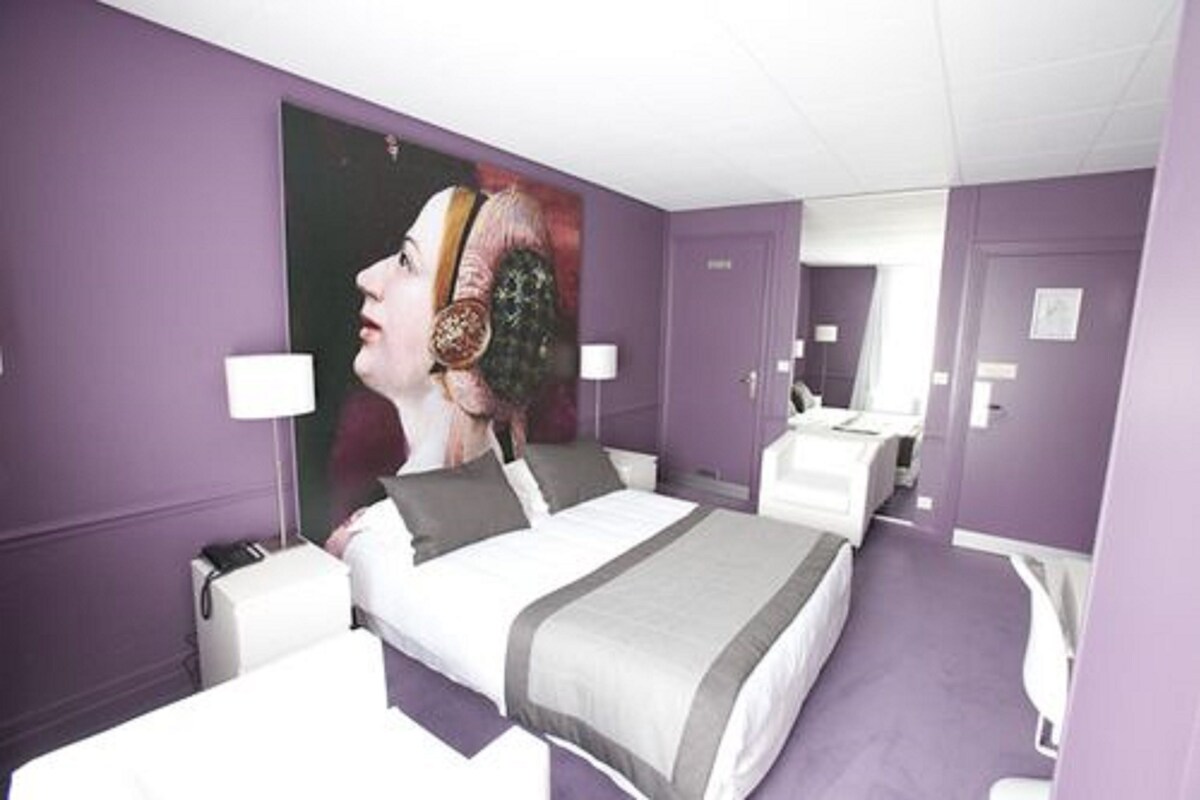A hotel room with a bed, bedside tables, a mirror, and a large poster on the wall.