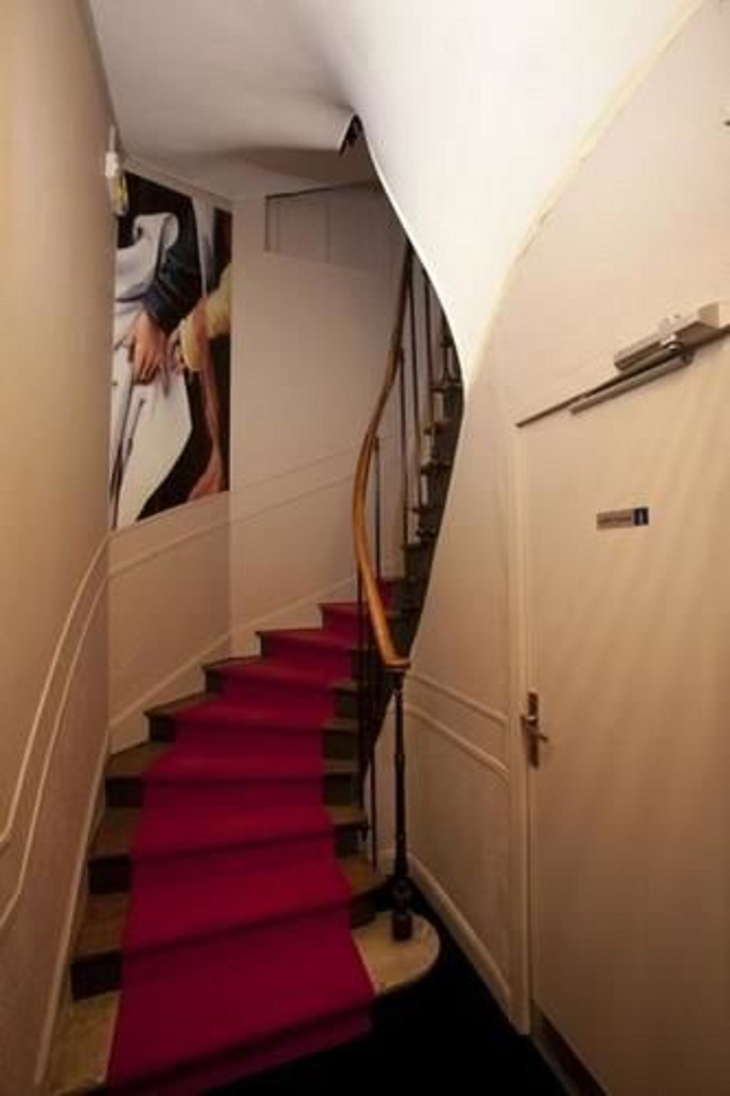 Una escalera con alfombra roja, barandilla y una puerta con un letrero.