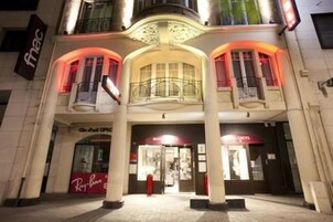 L’entrée d’un hôtel, avec un balcon central, une enseigne Ray-Ban et une enseigne « HÔTEL » au-dessus des portes.