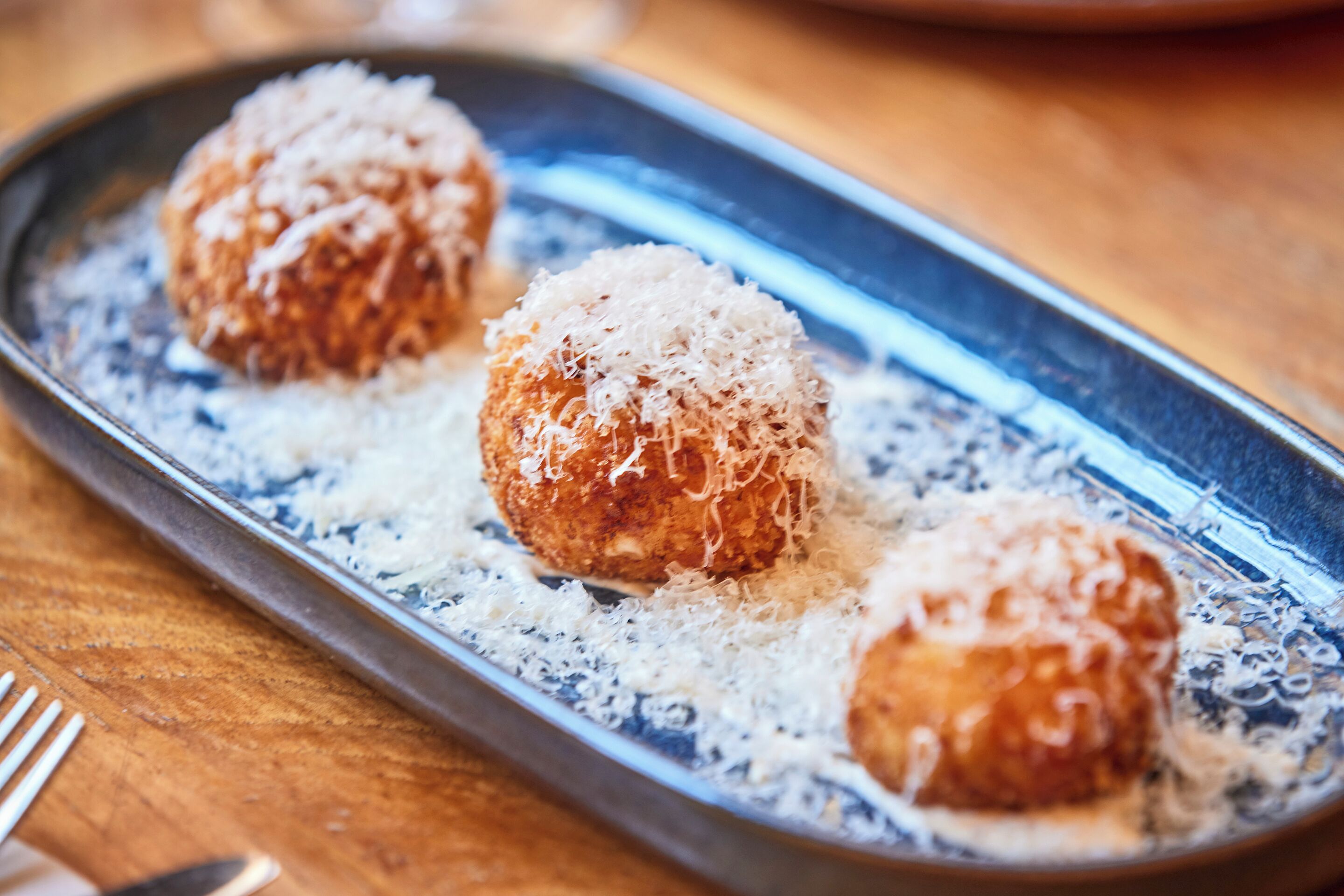 A dish with three round, golden-brown balls topped with shredded coconut, served on a blue and white patterned plate.