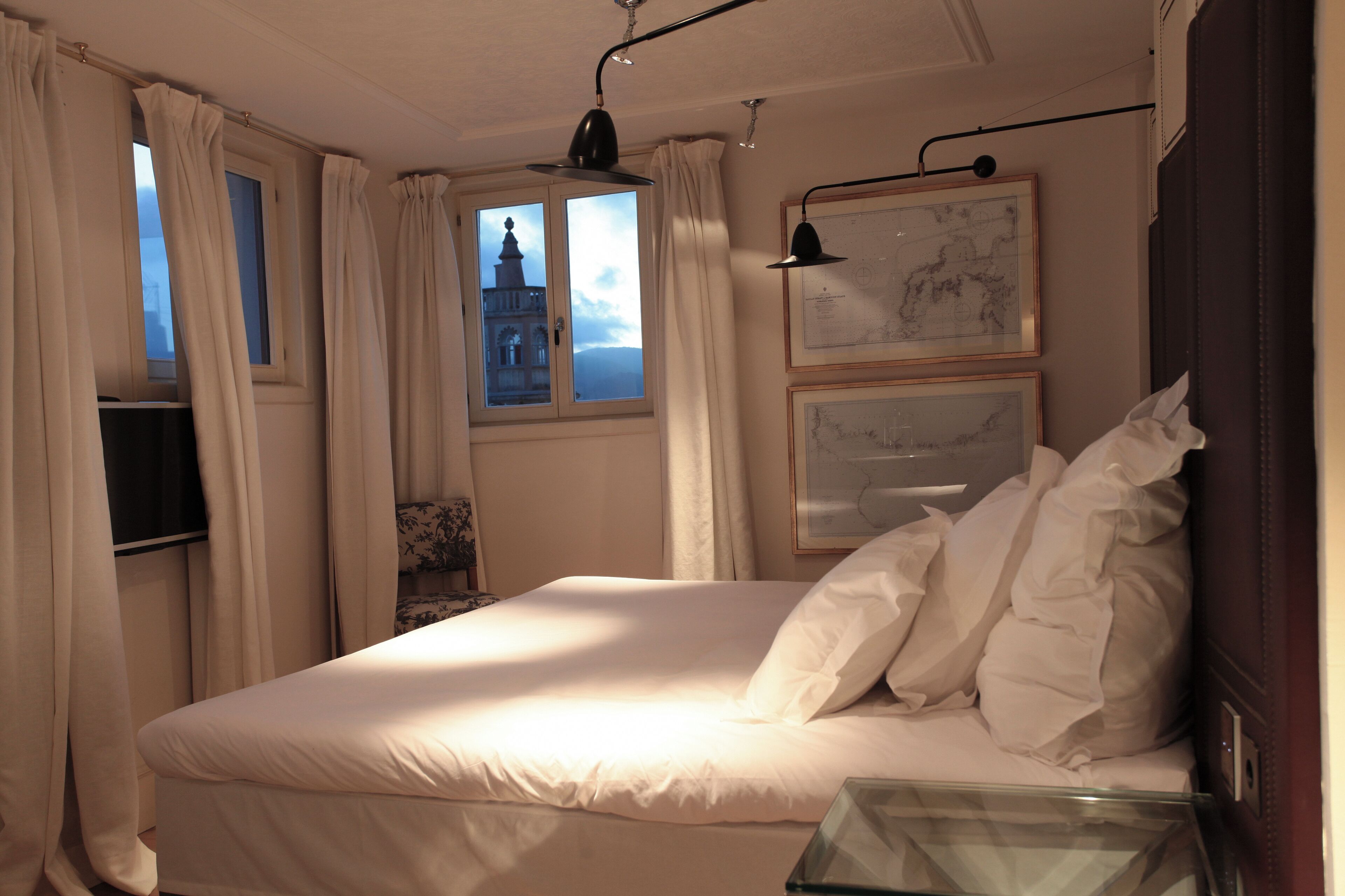 A neatly made bed with white linens, a window with curtains, and framed artwork on the wall.