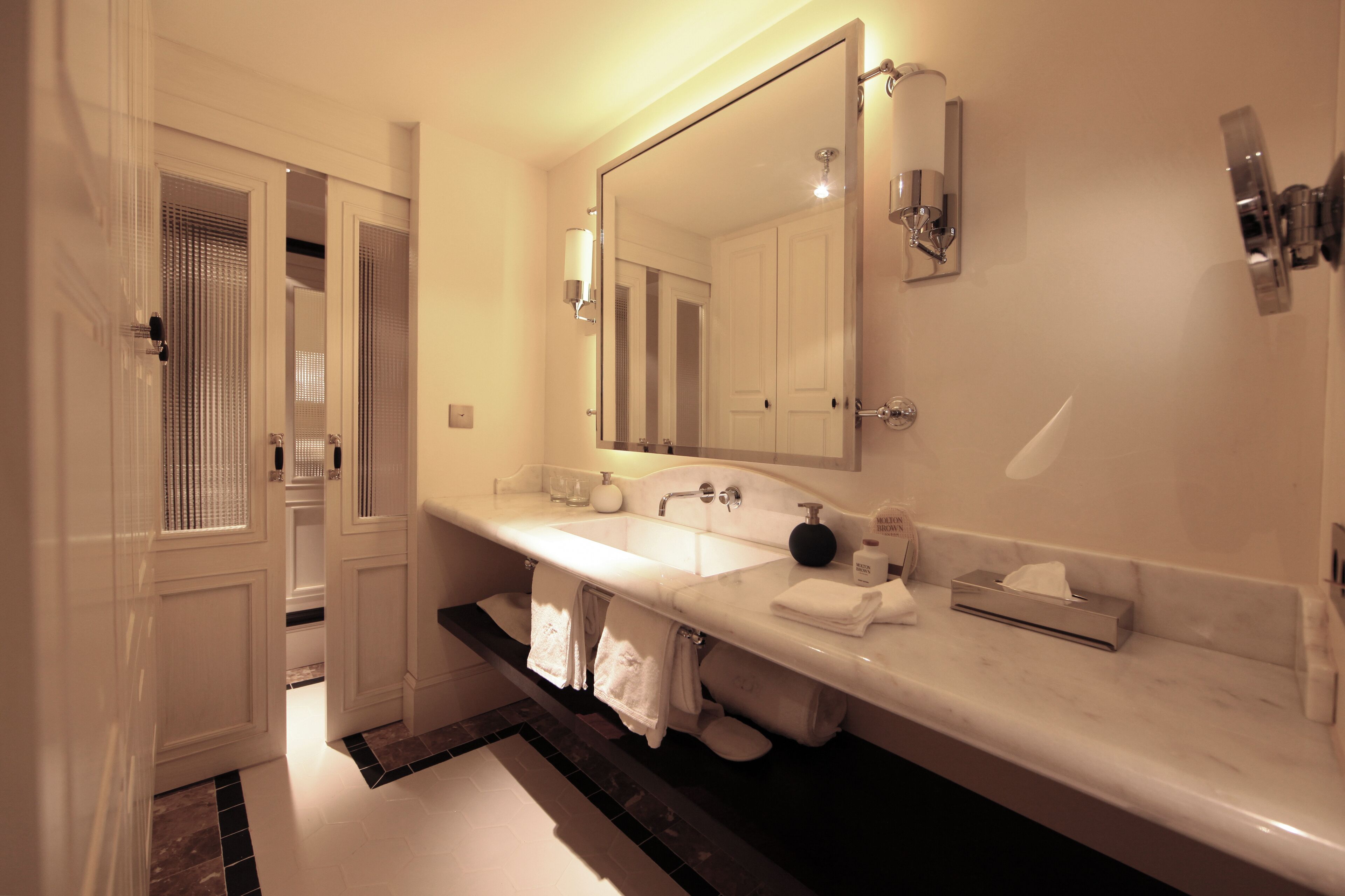 Un baño moderno con un espejo grande, dos lavamanos y un perchero para toallas.