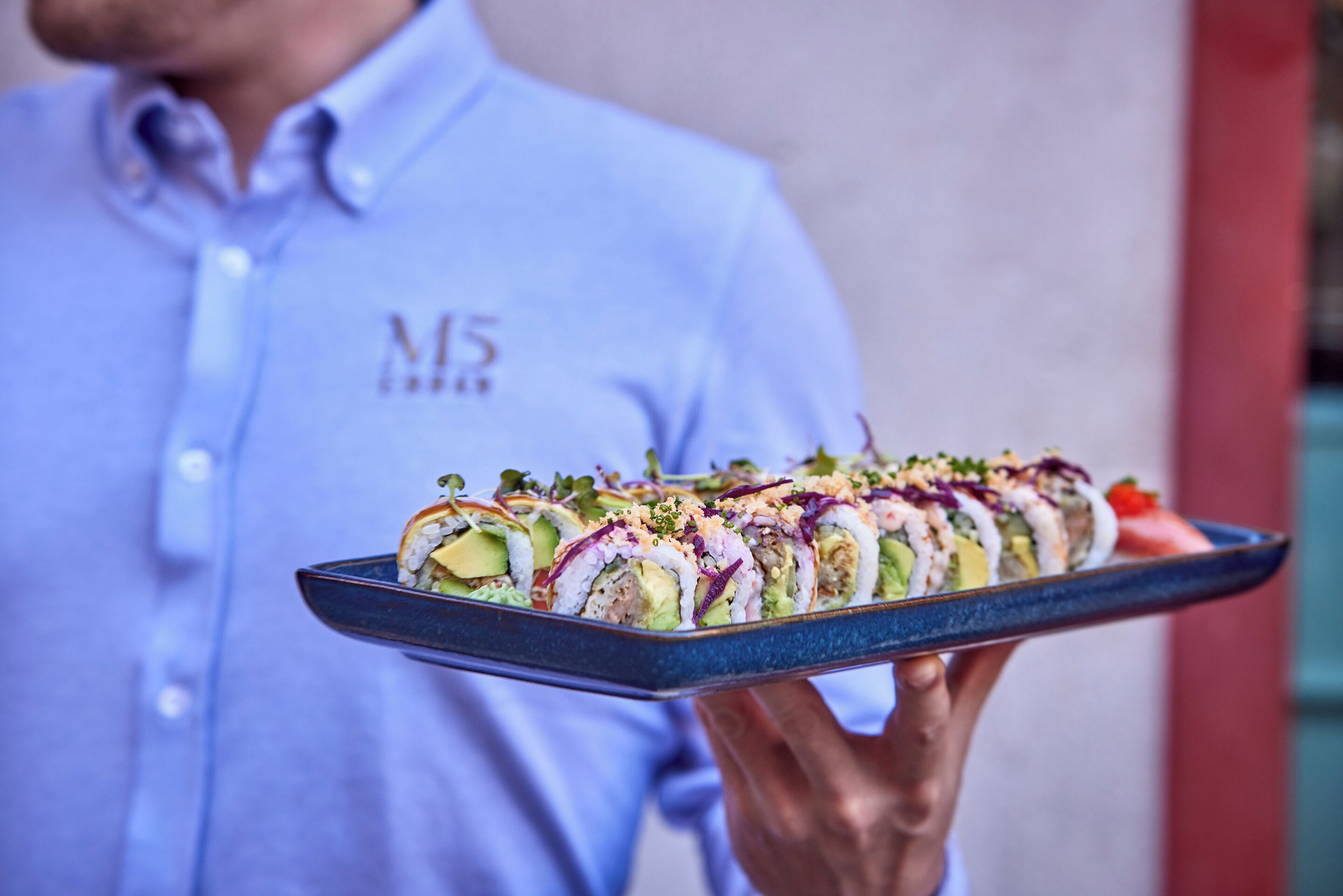 Una persona sosteniendo una bandeja con un rollo de sushi.