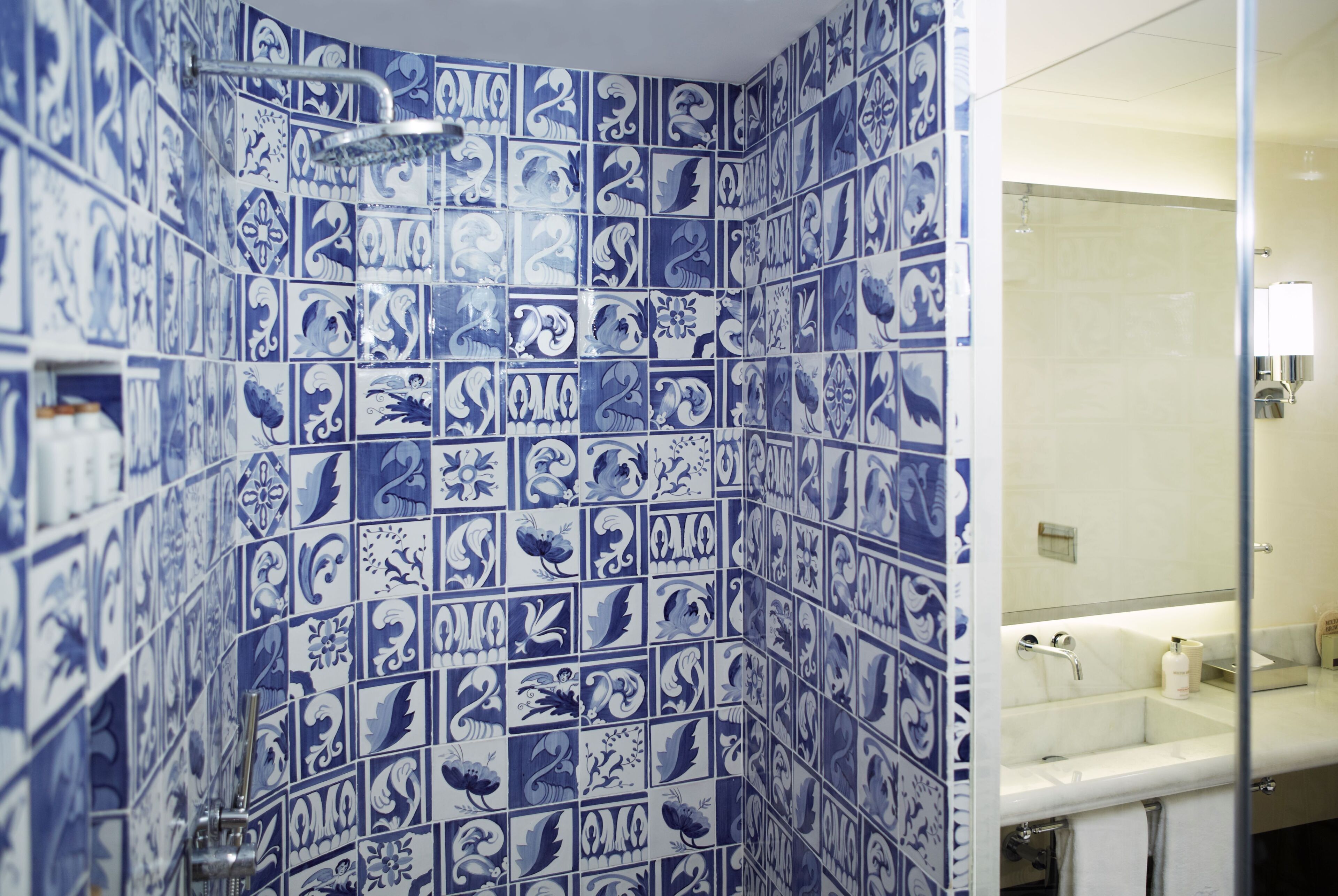 Un baño con azulejos blancos y azules estampados, un lavamanos blanco y un espejo.