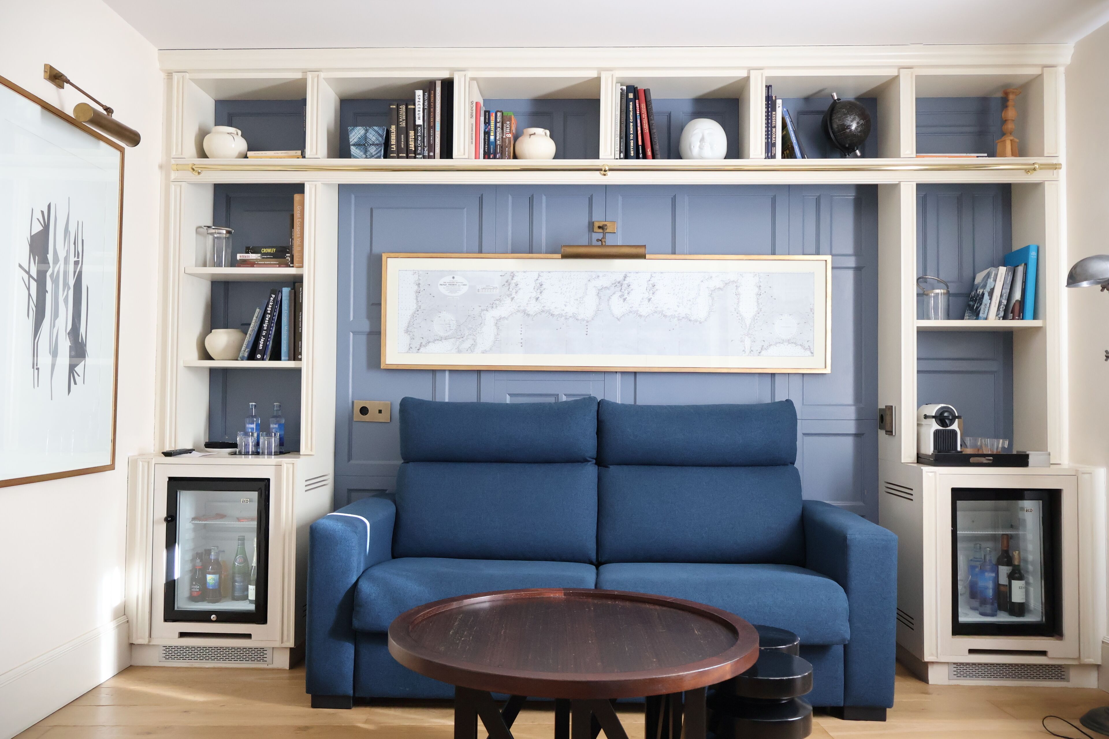 A modern living room with a blue sofa, a round wooden coffee table, and built-in shelving with books and decorative items.