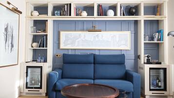 A modern living room with a blue sofa, a round wooden coffee table, and built-in shelving with books and decorative items.