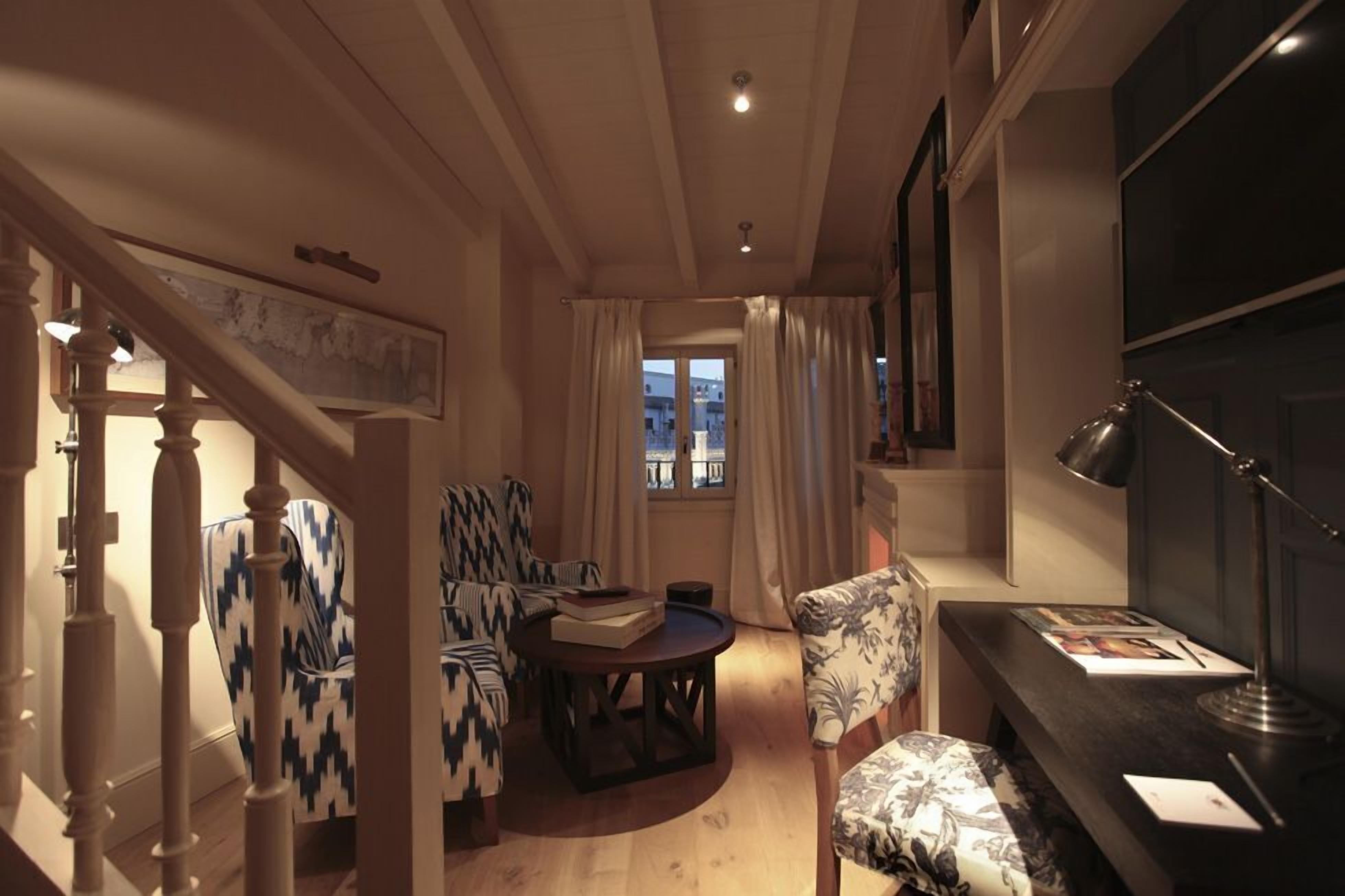 Una sala de estar acogedora con una escalera, una mesa redonda de centro, sillones estampados y un escritorio con una lámpara.