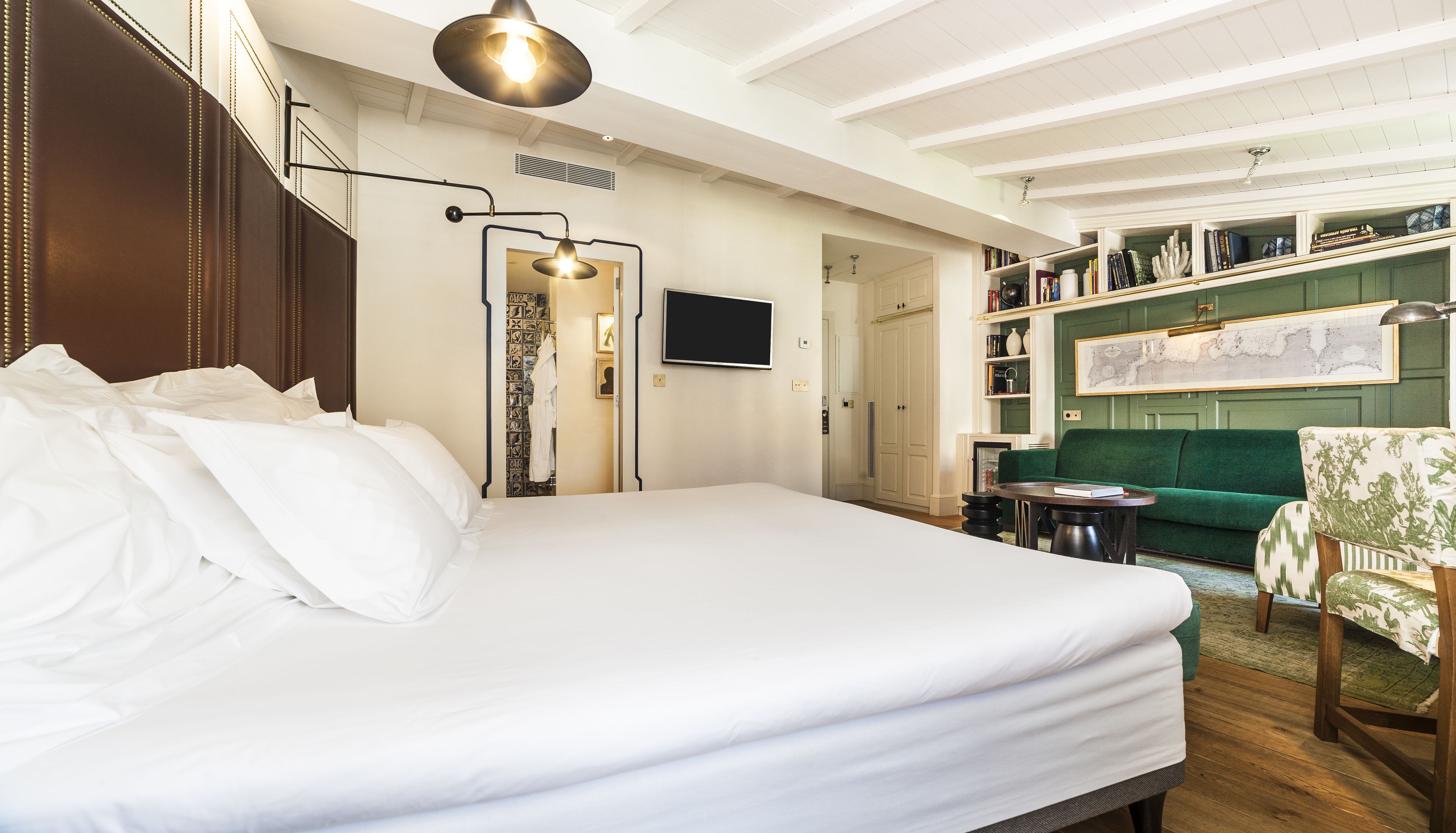 A hotel room with a large bed, a television, a green sofa, and a bookshelf.