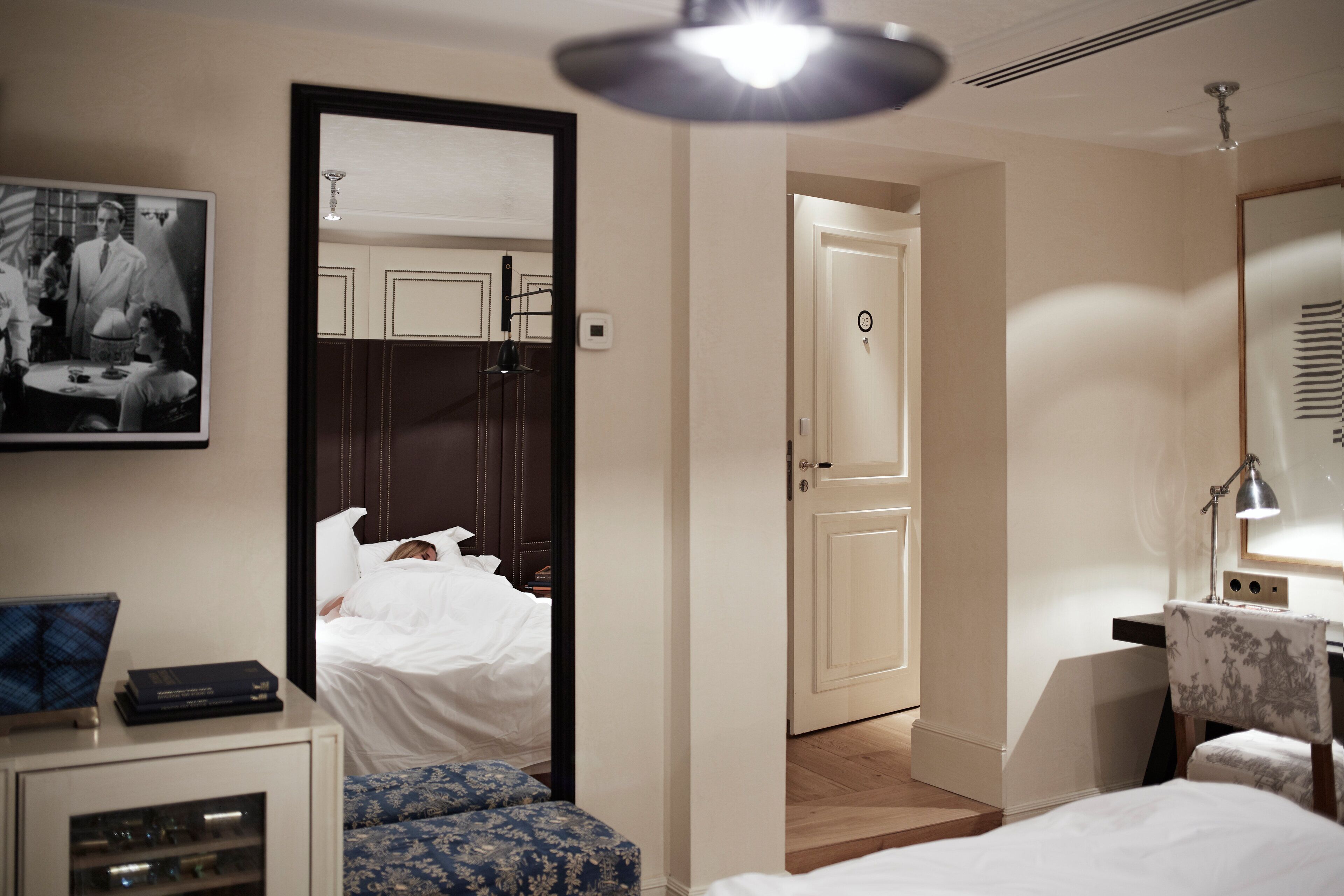 Une chambre d’hôtel avec un lit, un bureau, une chaise, un miroir, une armoire et un tableau au mur.