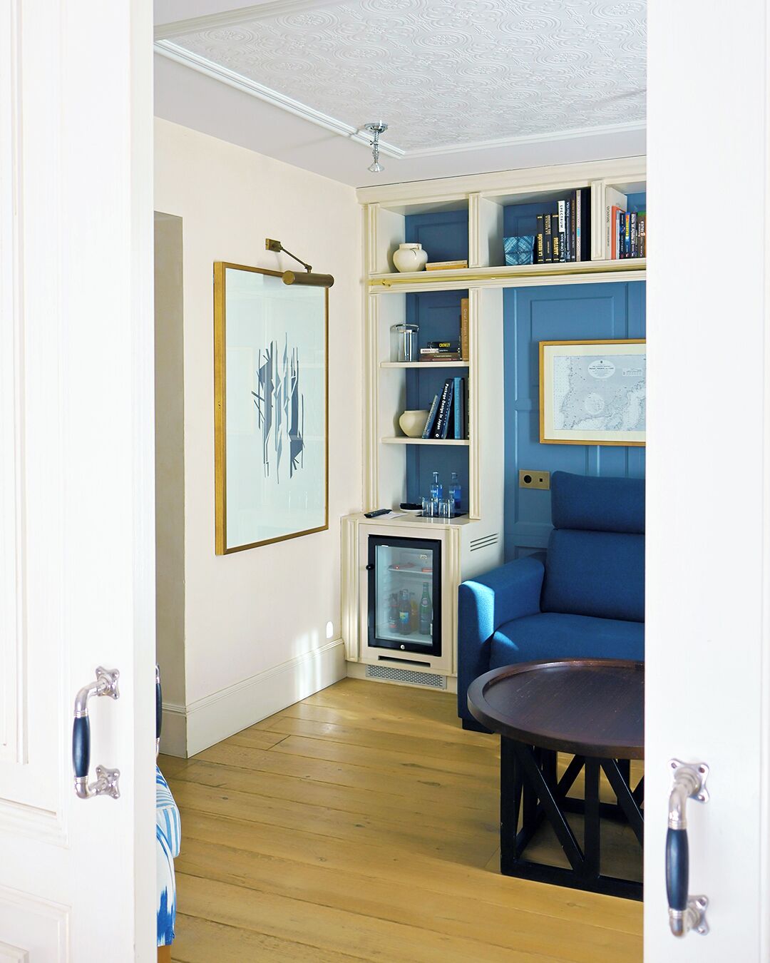 A room with a blue sofa, a small round table, a cabinet with shelves, and a framed picture on the wall.