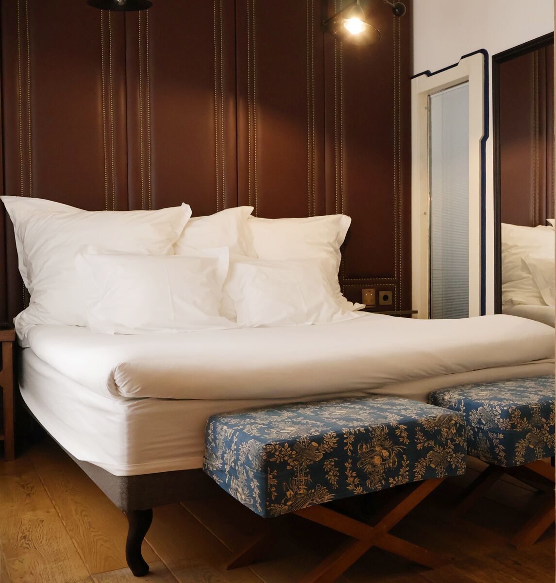 A neatly made bed with white linens and a blue patterned bench at the foot of the bed.