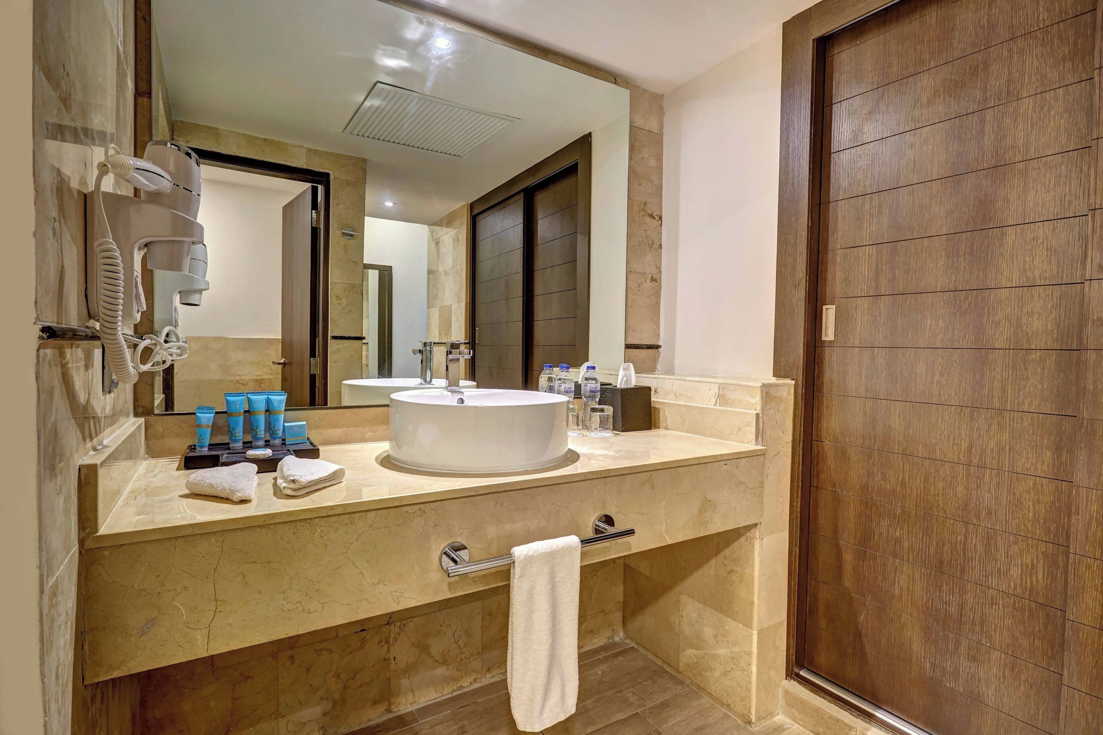 Un bagno con un ampio specchio, due lavandini, un asciugacapelli e articoli da toilette sul ripiano.