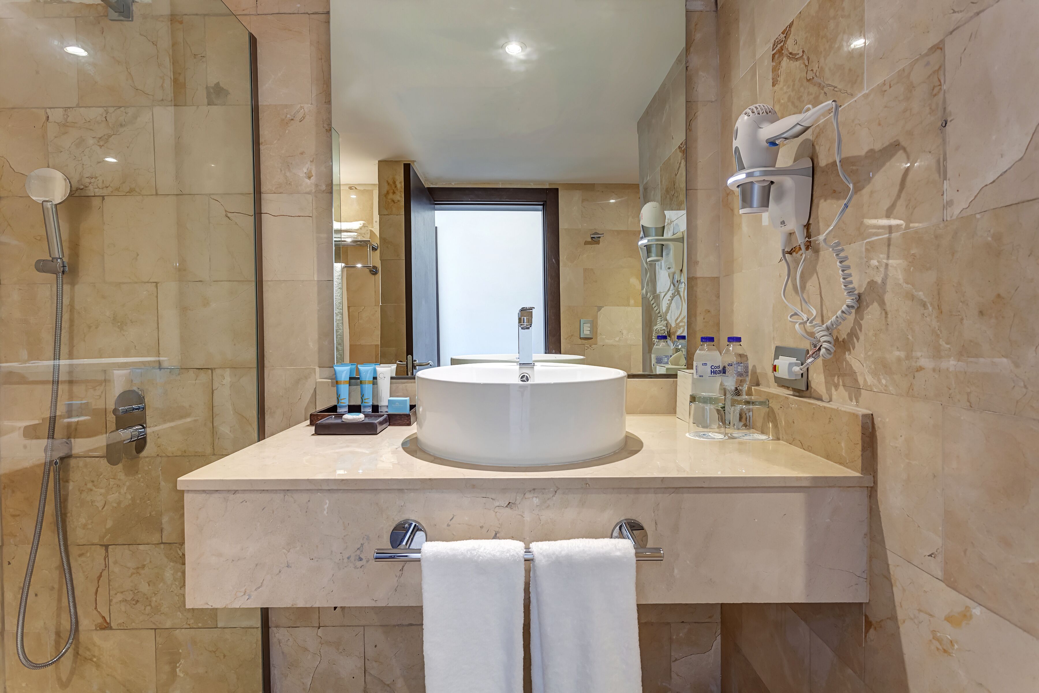 A modern bathroom with a round sink, a handheld showerhead, and a hairdryer mounted on the wall.