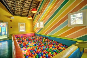 Un área de juegos interior colorida con piscina de pelotas, paredes a rayas y un tobogán.