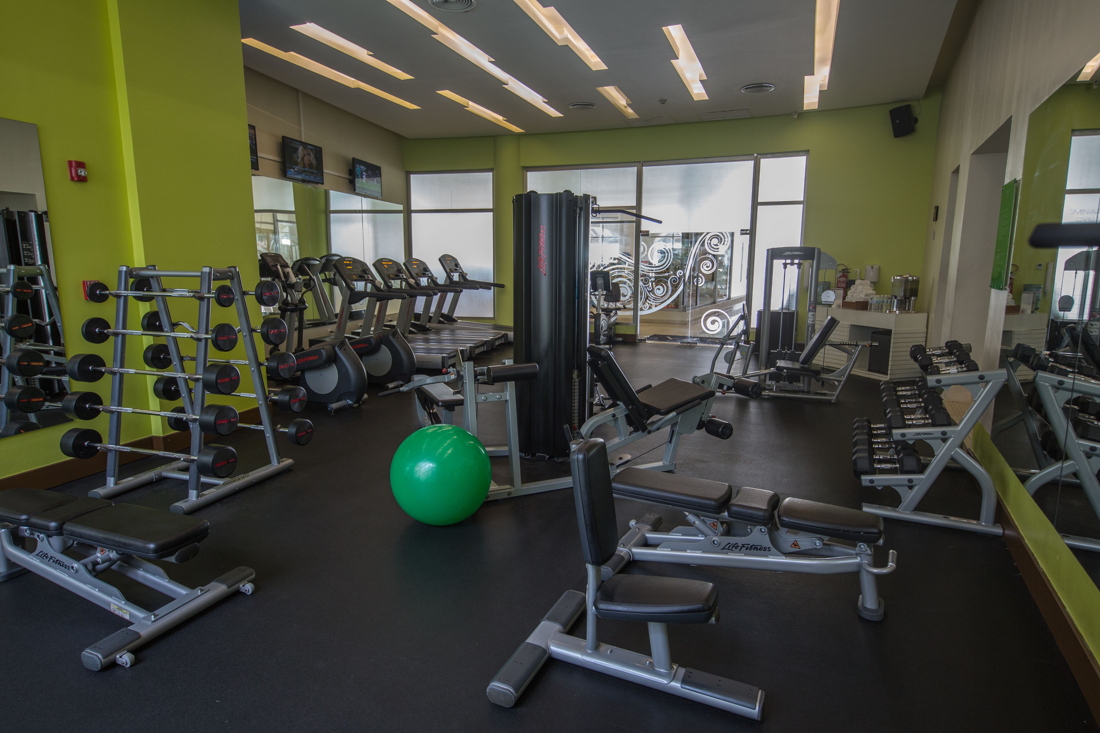 A gym with various exercise equipment, a green exercise ball, and a mirror on the wall.