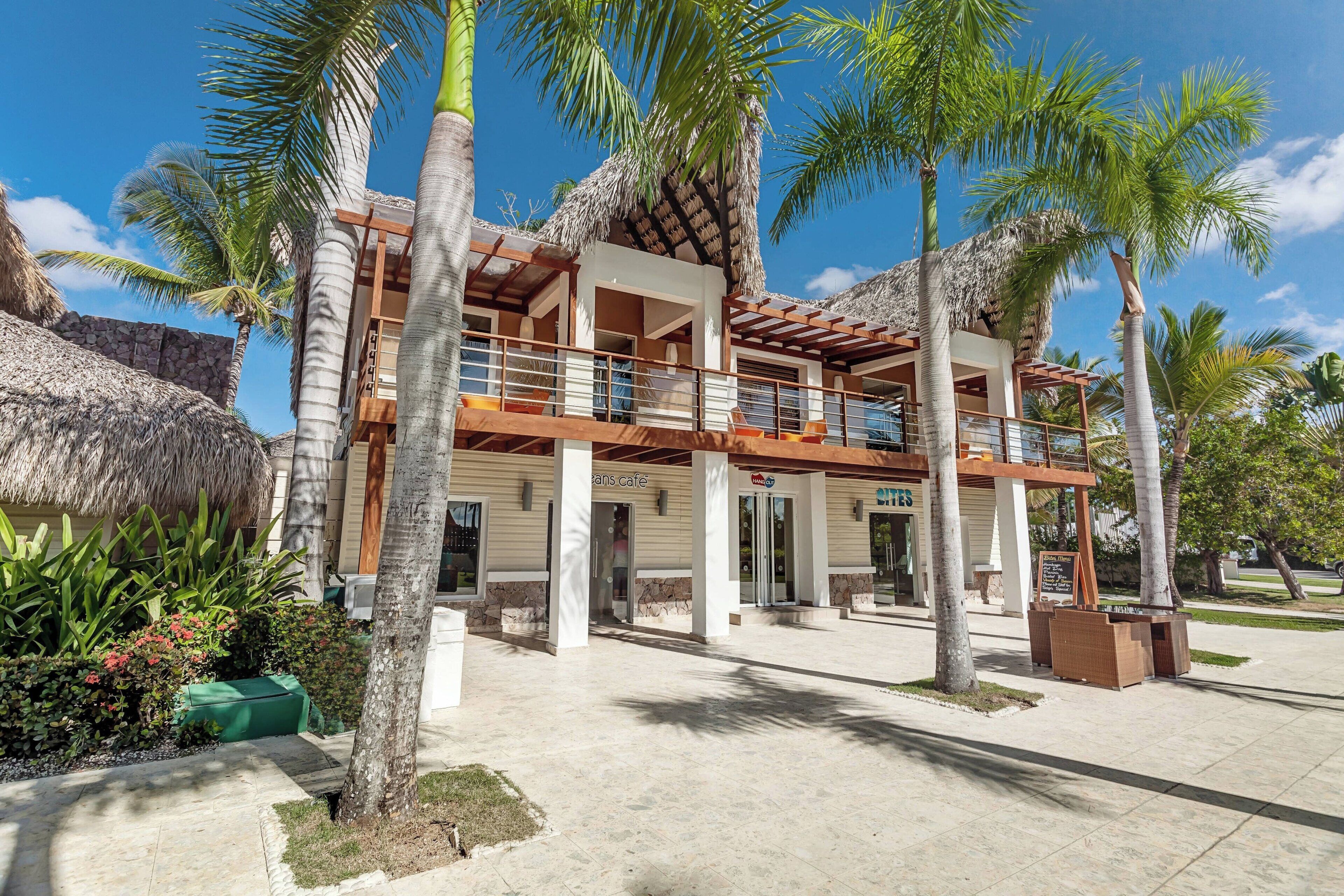 A resort with a two-story building, outdoor seating area, and palm trees.