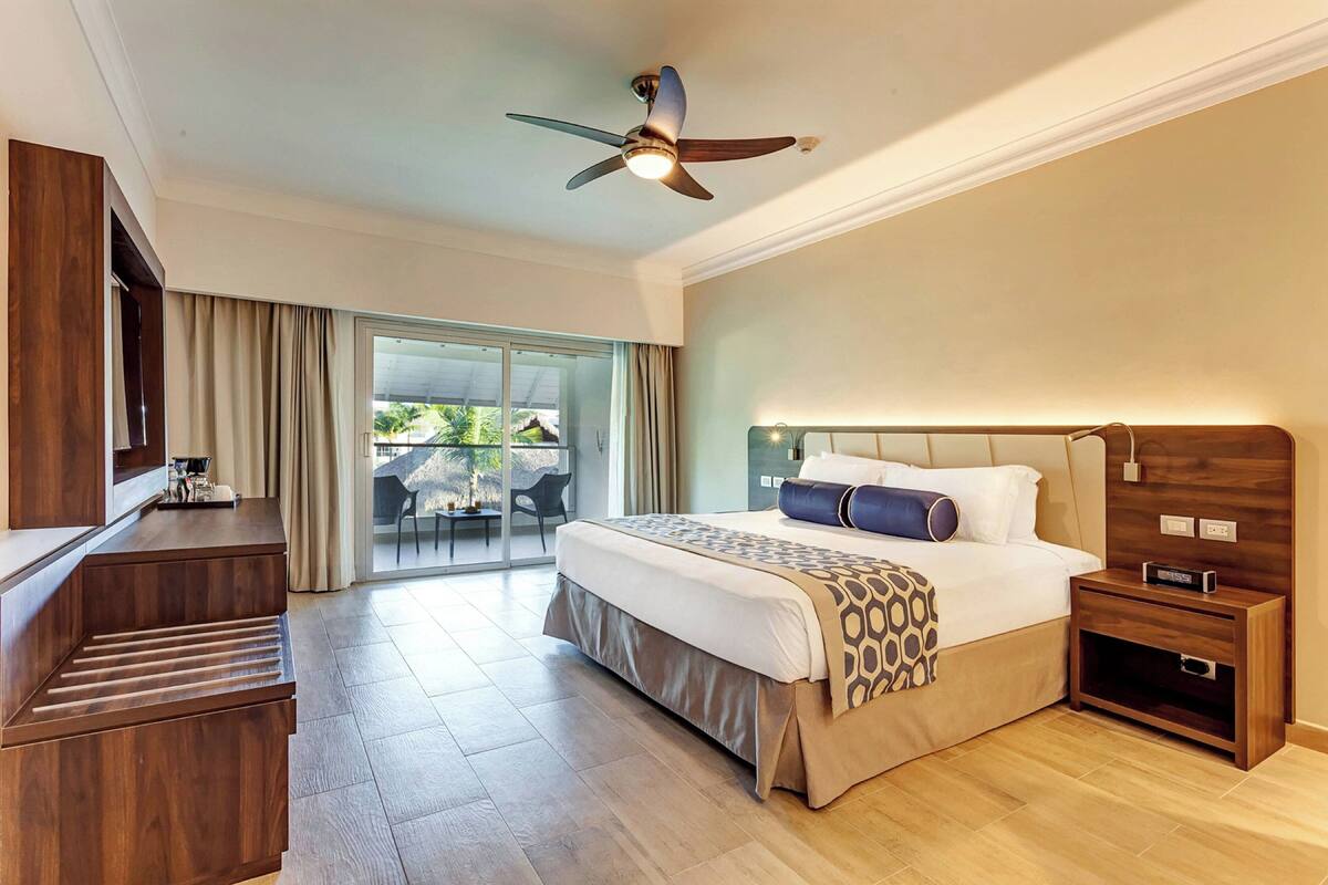 A hotel room with a bed, bedside table, TV, and a ceiling fan.