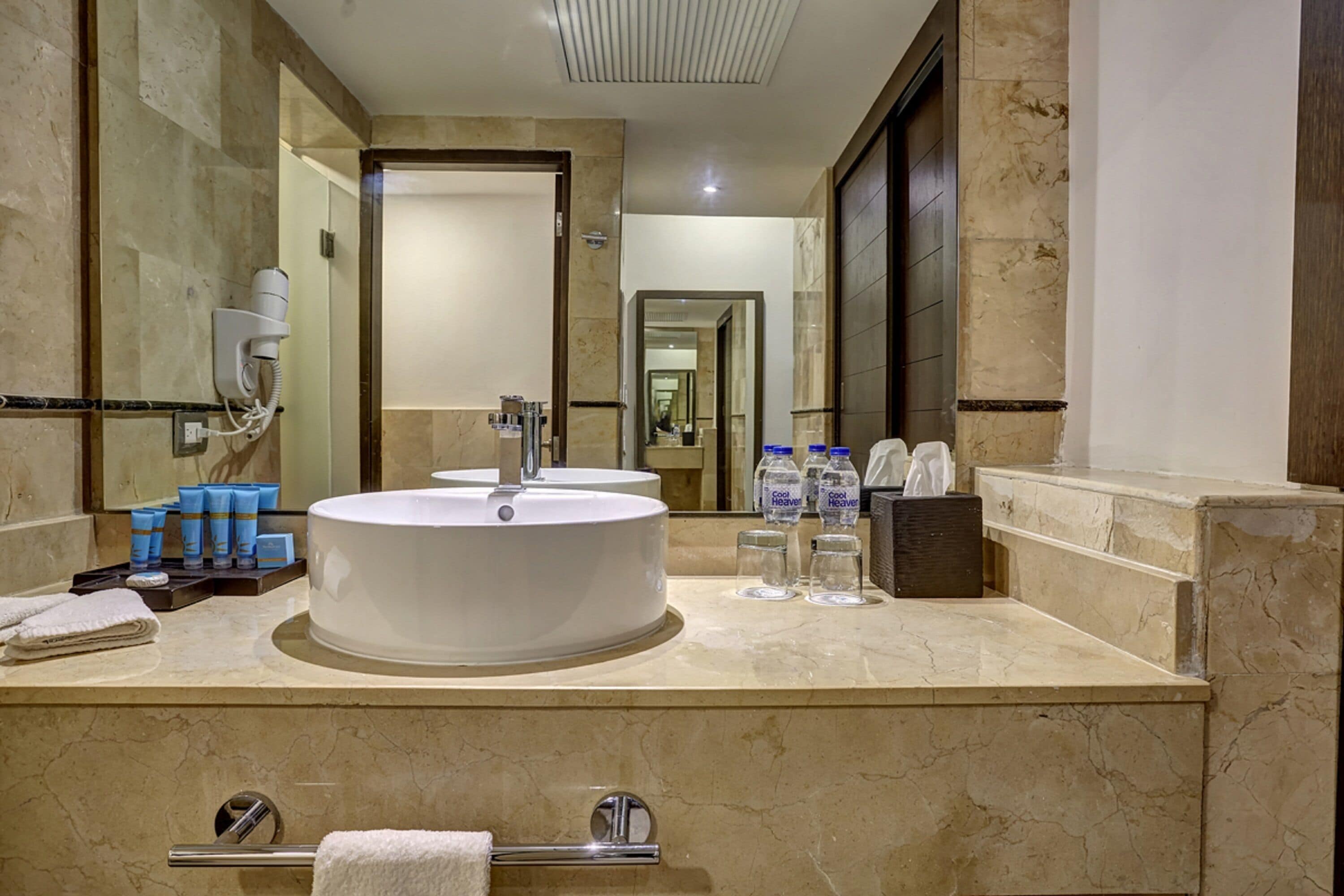 A modern bathroom with a large round sink, a mirror, and a hairdryer mounted on the wall.