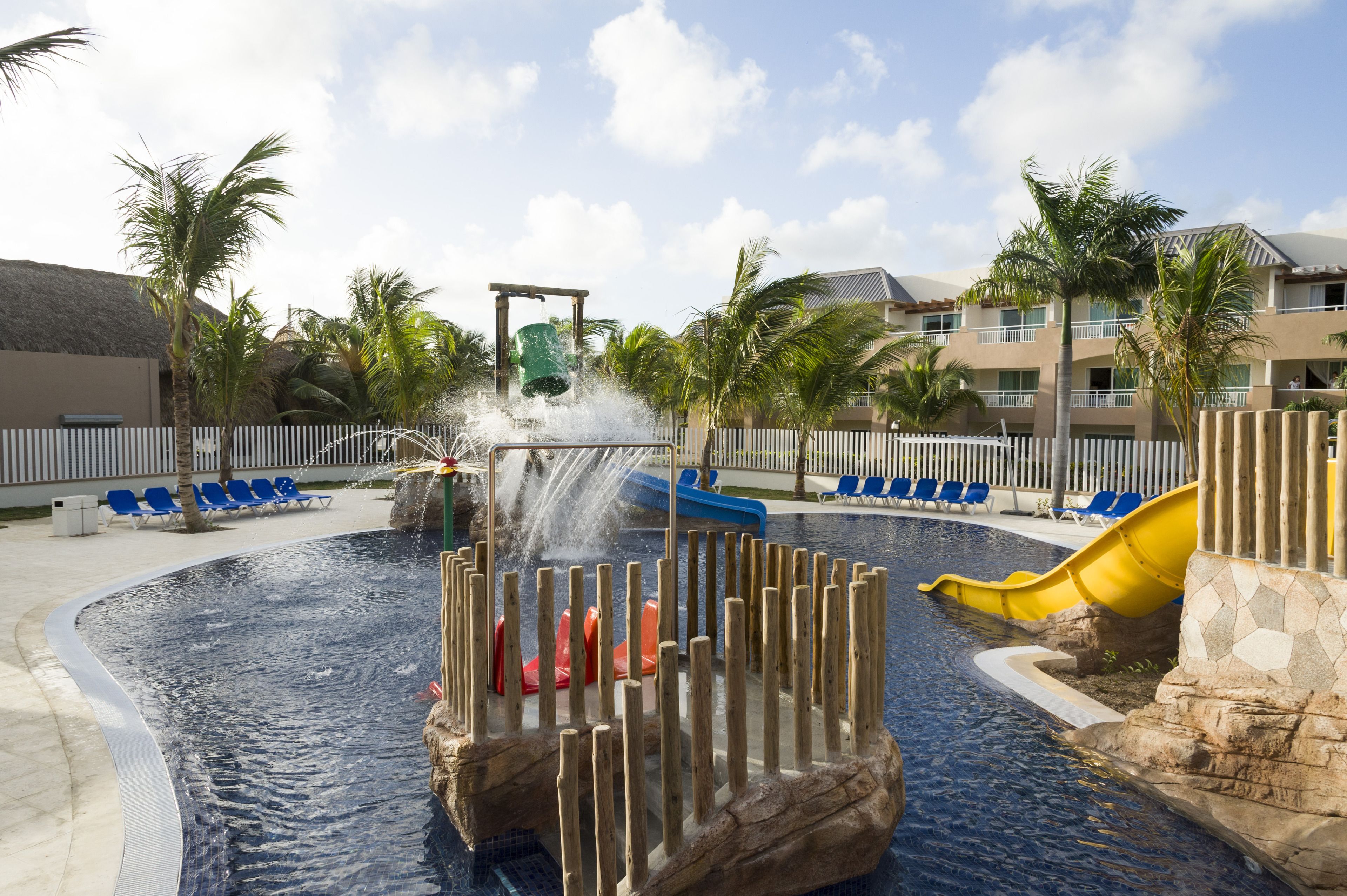 A water play area with slides and a pool, surrounded by palm trees and lounge chairs.