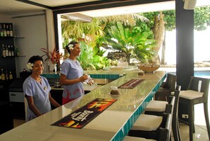 A bar area with a tropical view, a counter with a menu, and a seating area with wicker chairs. - Garden Island Resort (Taveuni Island East)