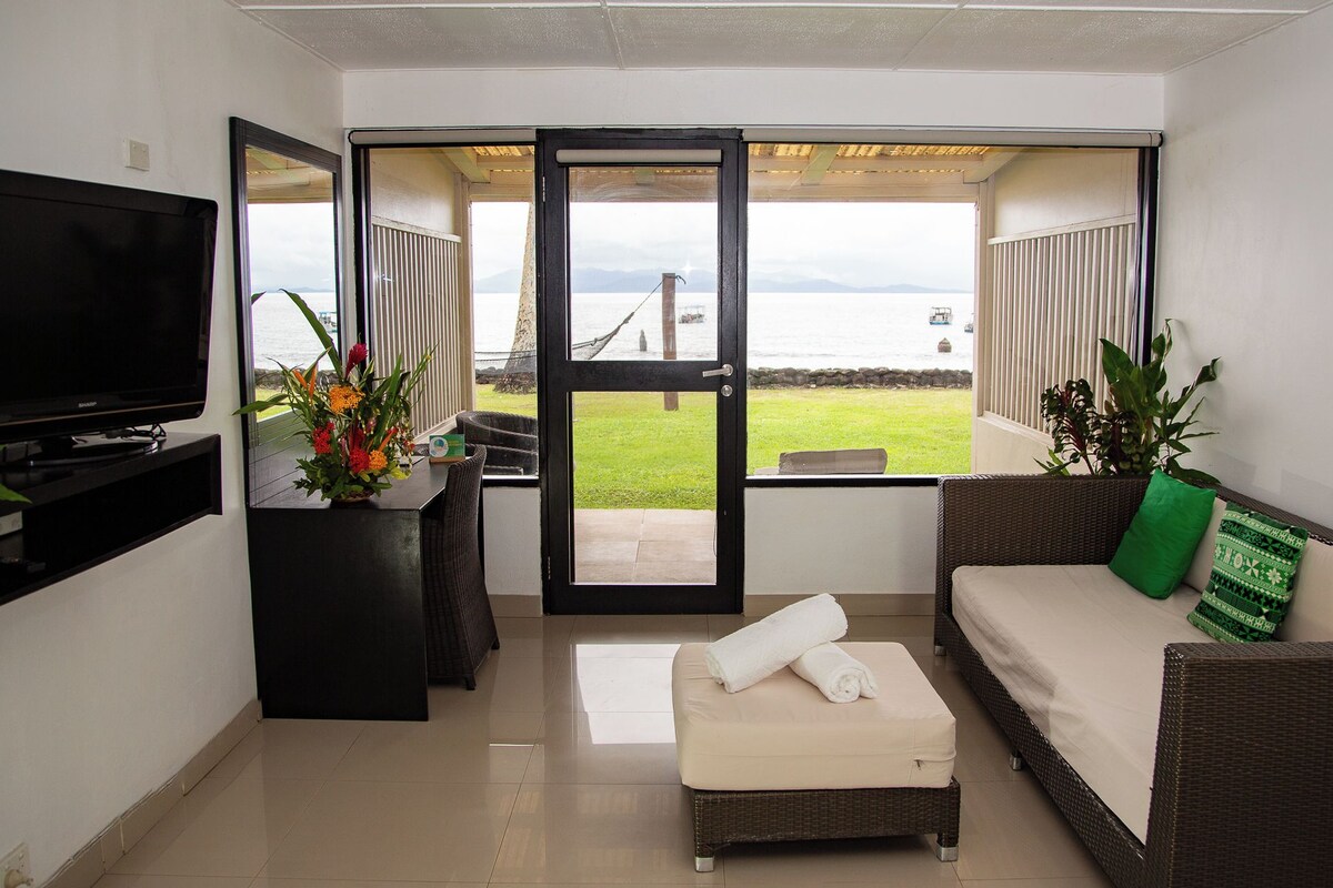A room with a television, a sofa, a small table, and a view of the sea through a glass door.